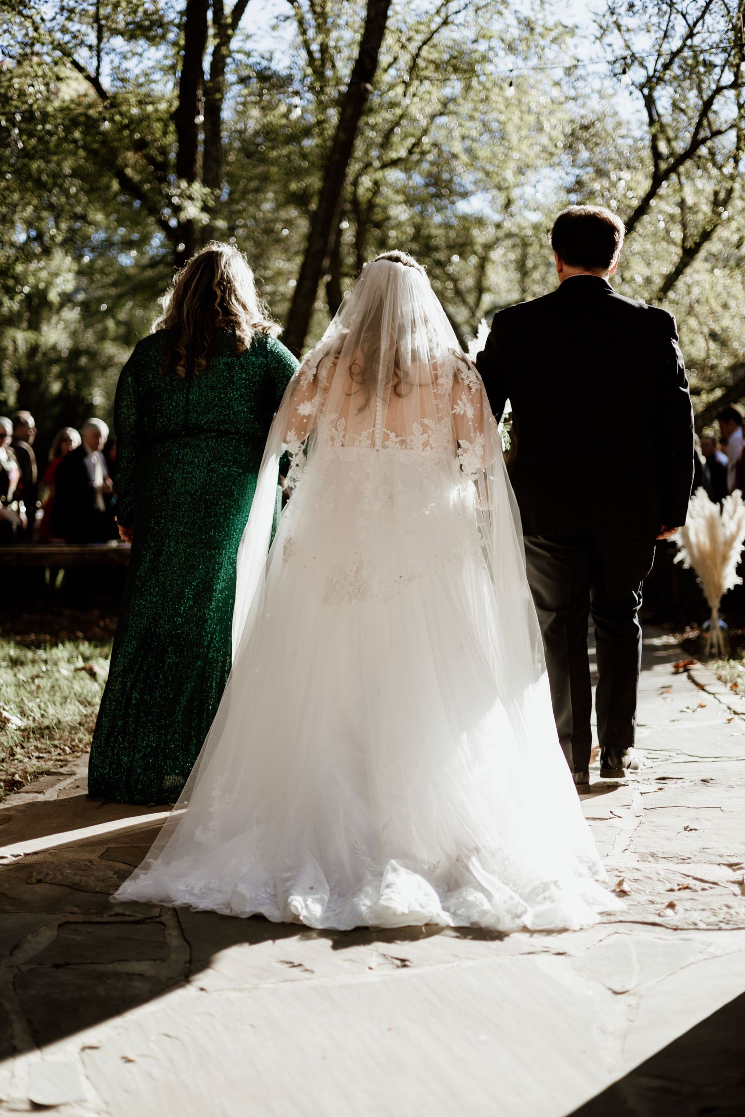Back view of bride in flowing white gown and veil during outdoor ceremony.