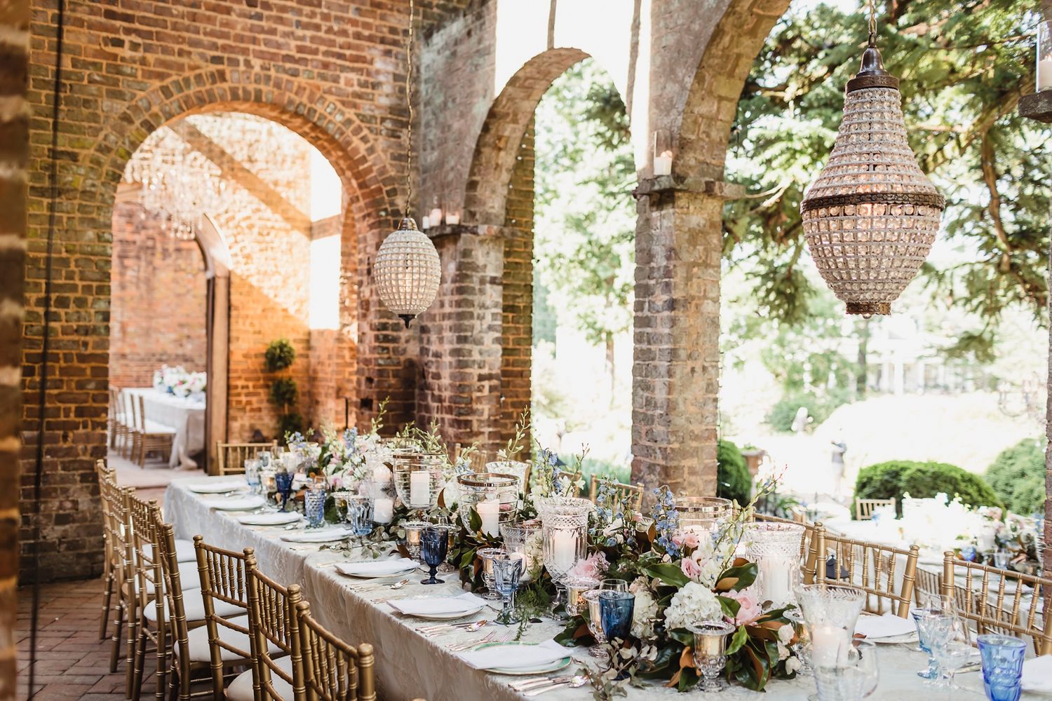 Elegant wedding reception venue with exposed brick walls, crystal chandeliers, and floral centerpieces on round tables.