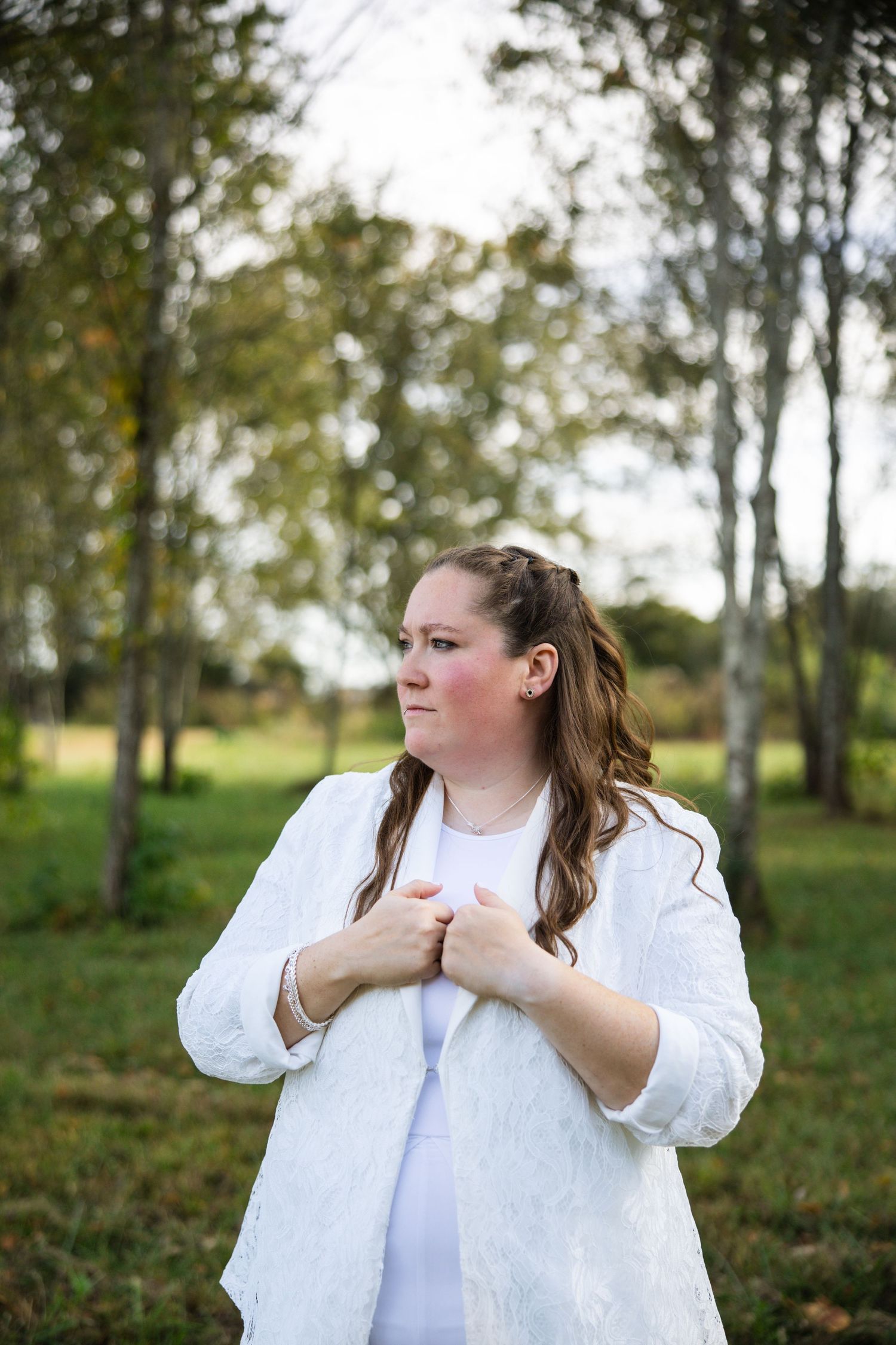 A person in a white button-up shirt stands thoughtfully in a wooded area on an autumn day.