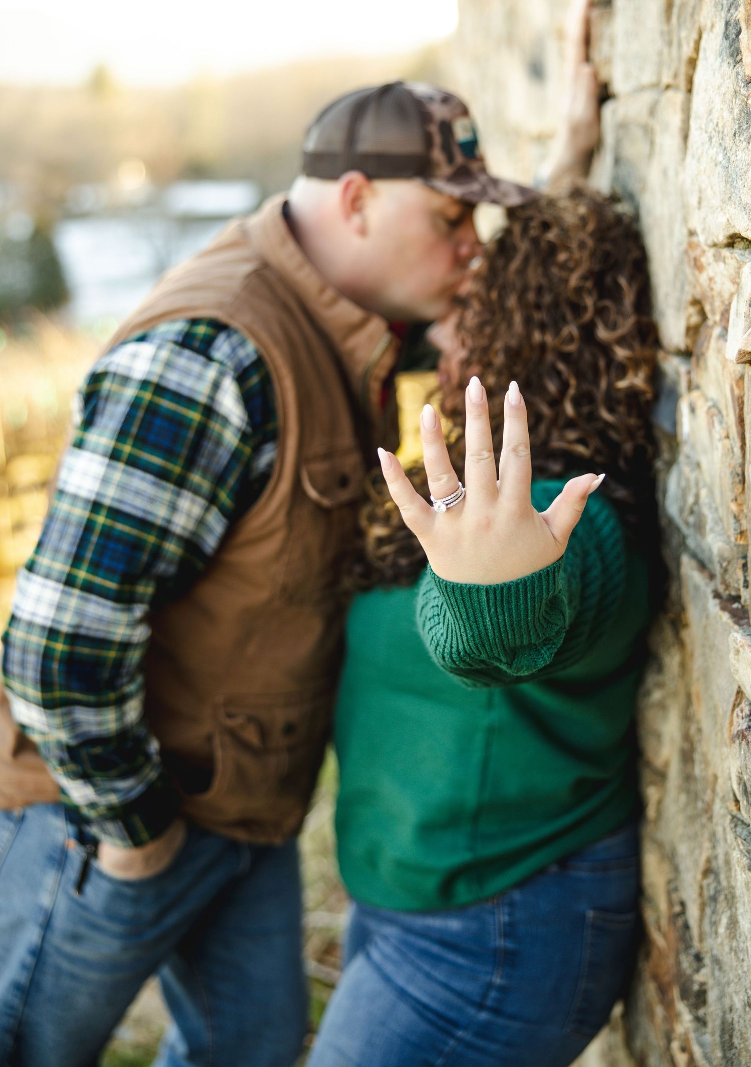 A couple in plaid and green sweater share an intimate moment against a wall.