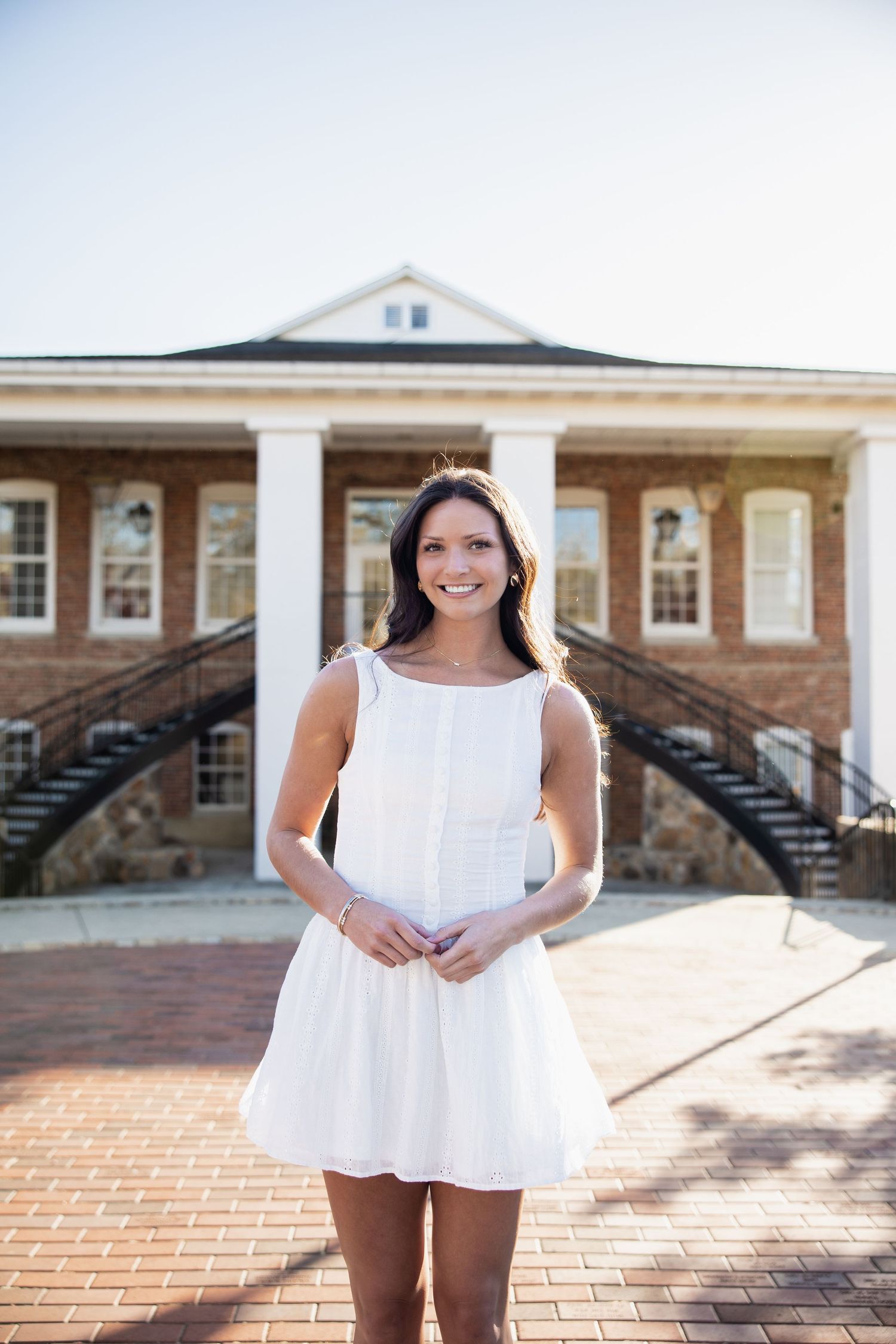 A white summer dress is worn in front of a historic brick building with symmetrical staircases.