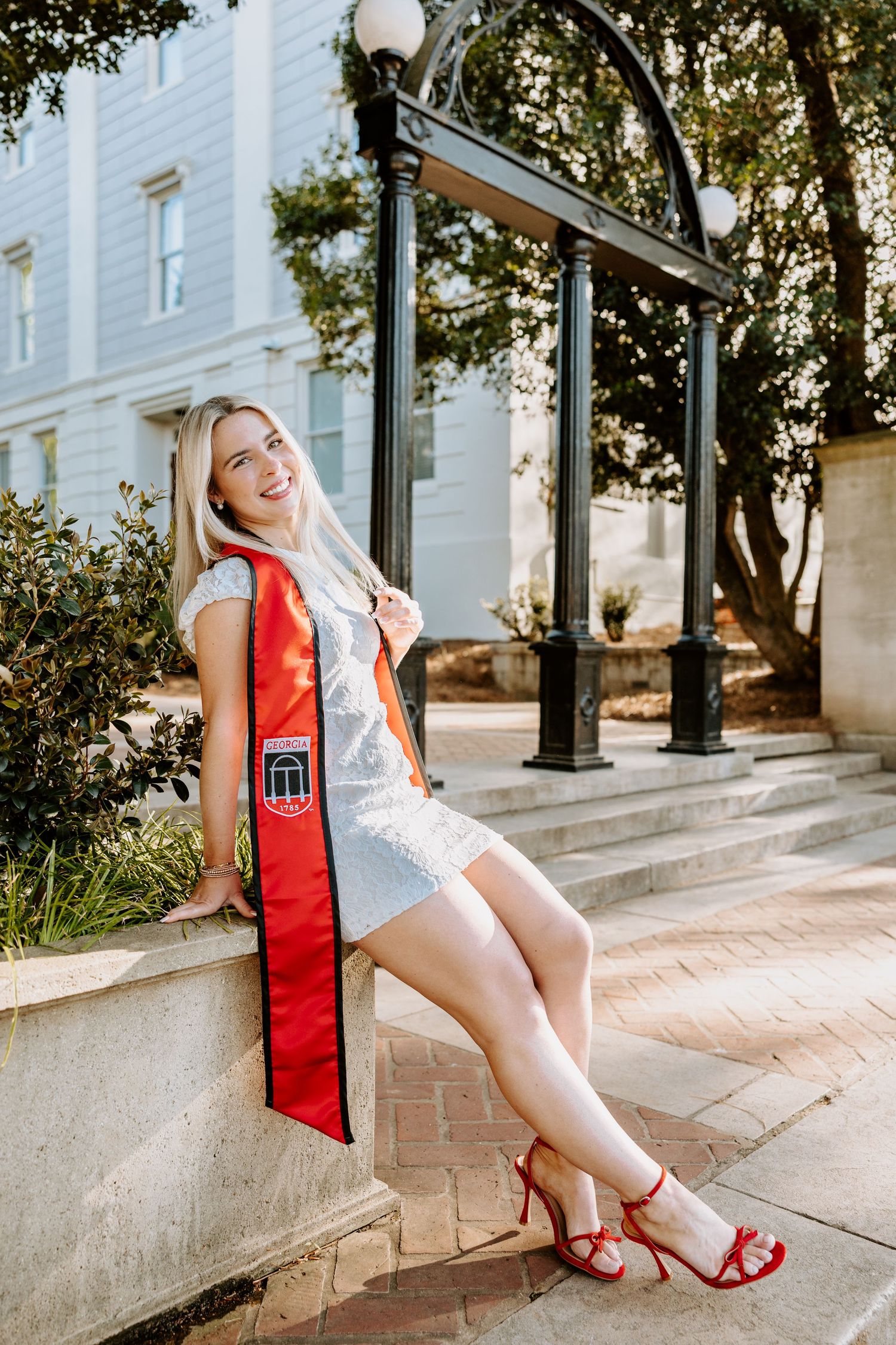 Graduate in red stole poses by University of Georgia arch landmark.