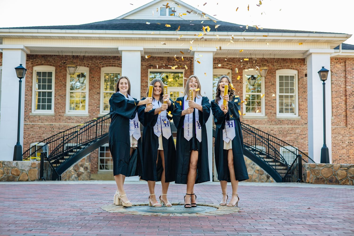 Group of graduates celebrating with champagne in front of collegiate building.