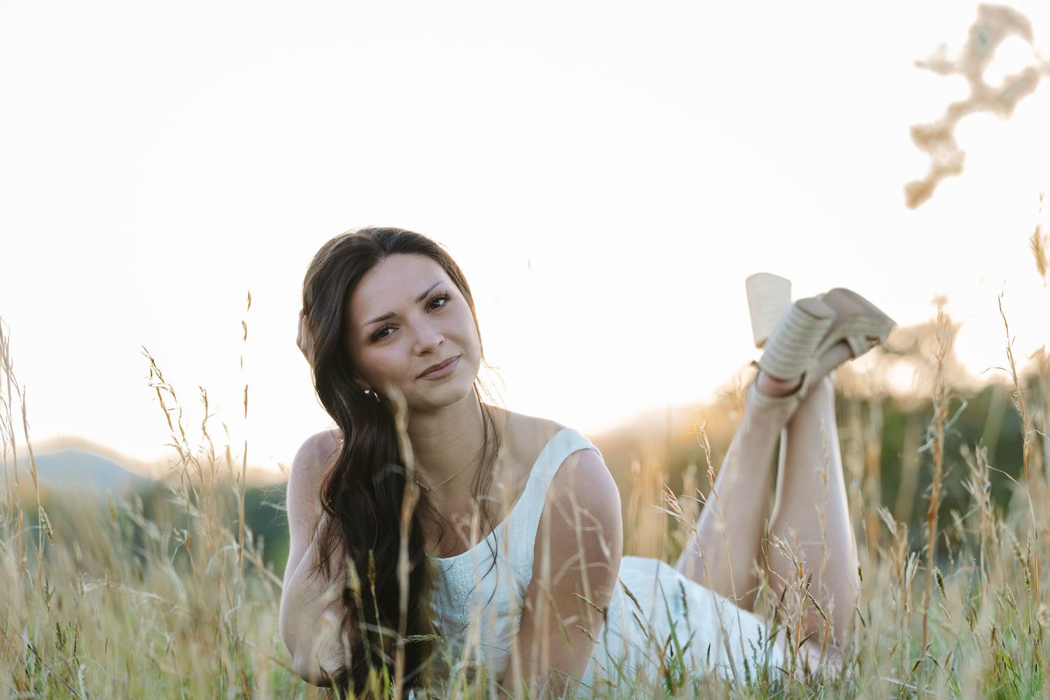 Person in white dress relaxing in mountain meadow at golden hour.