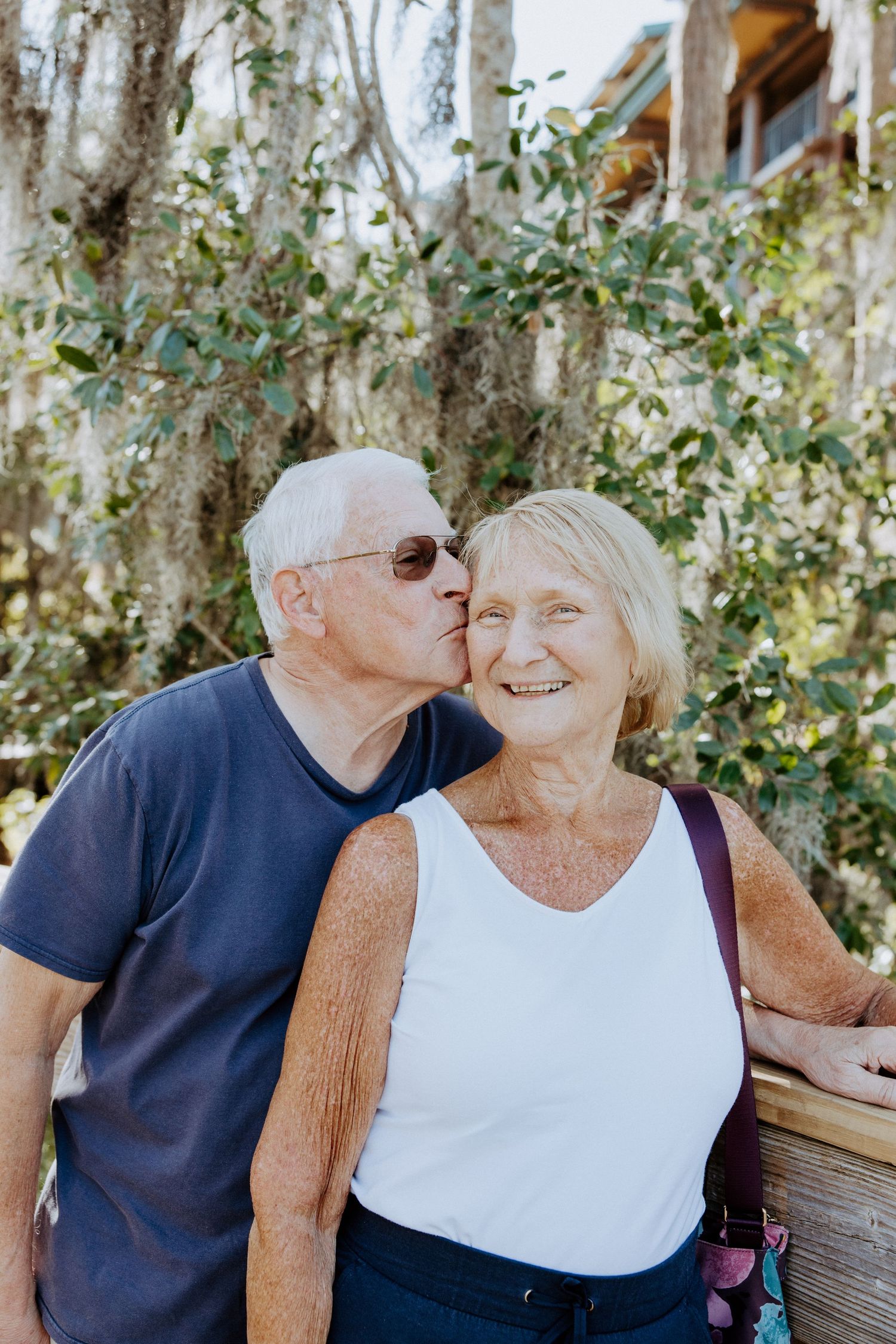 Intimate couple sharing sweet moments on a wooden bench surrounded by Spanish moss trees.