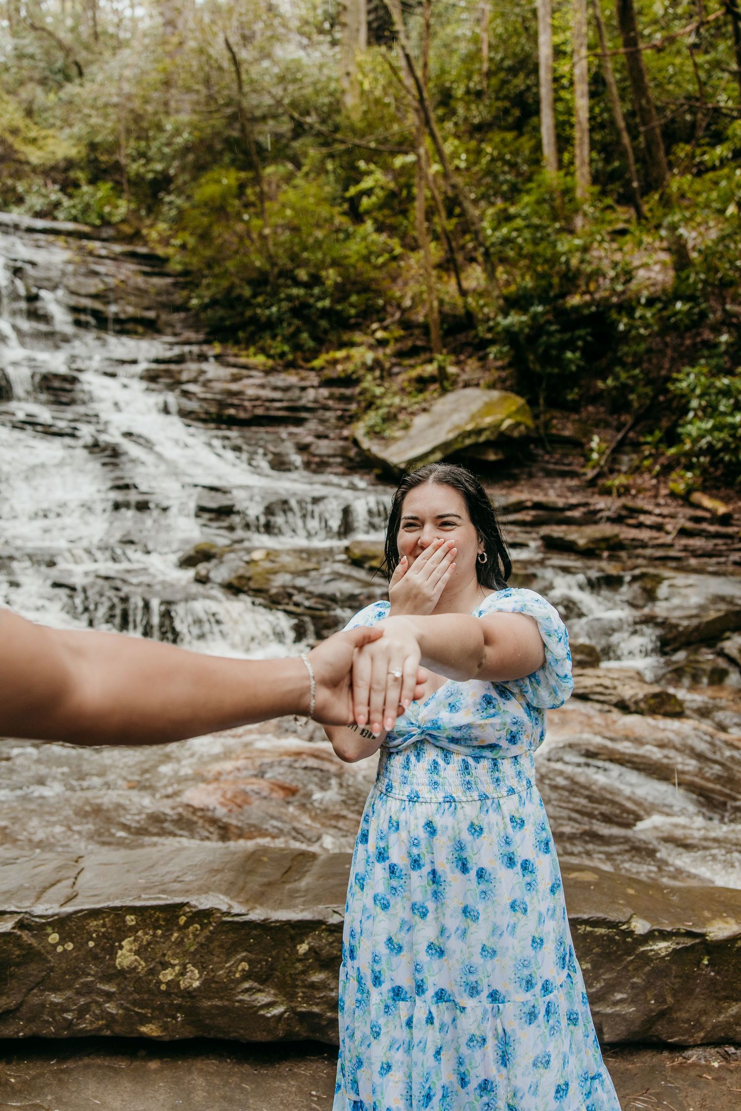 A surprised reaction captured in front of a waterfall while showing off an engagement ring.
