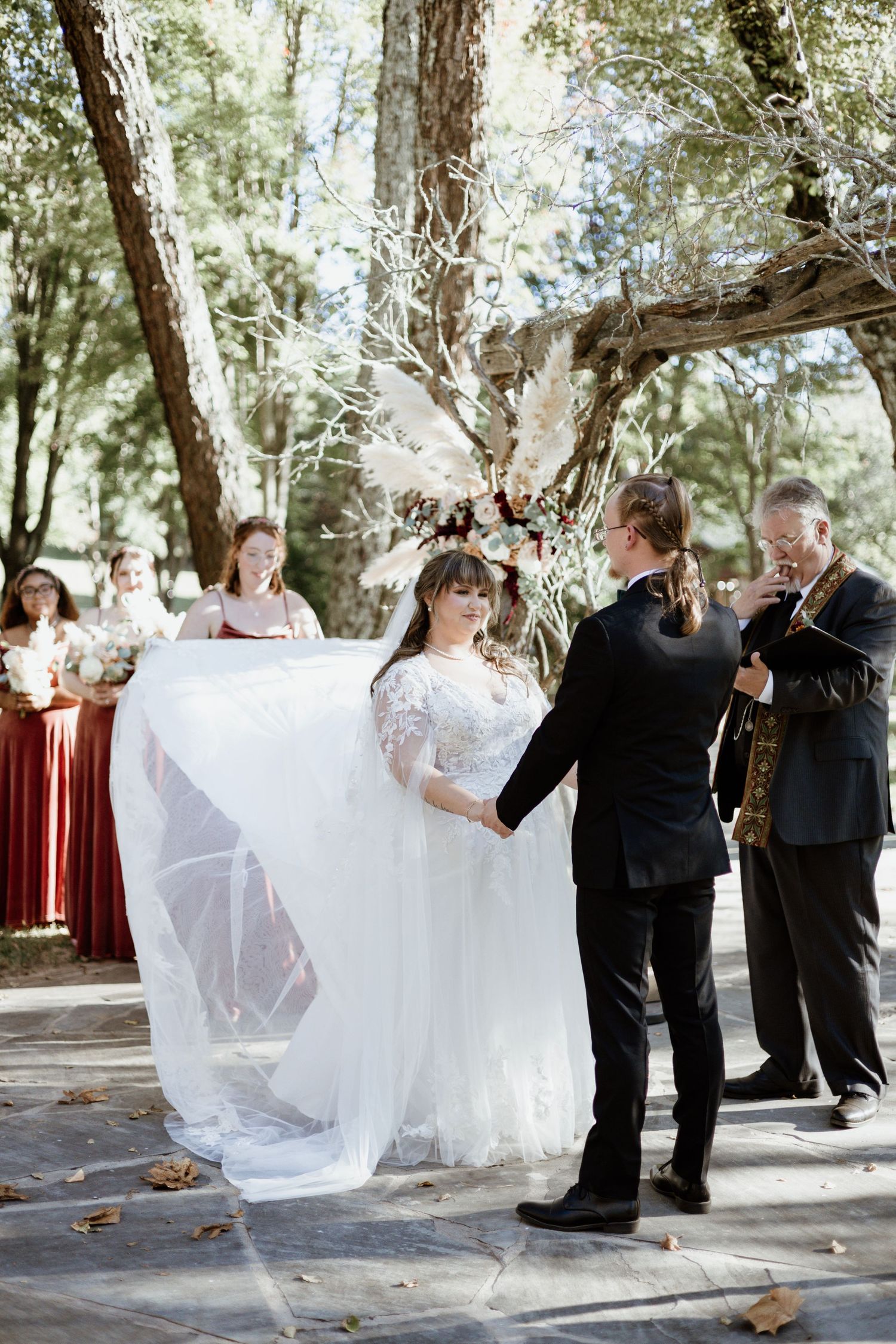 A beautiful outdoor wedding ceremony takes place in a wooded setting with a flowing white dress and burgundy bridesmaids.