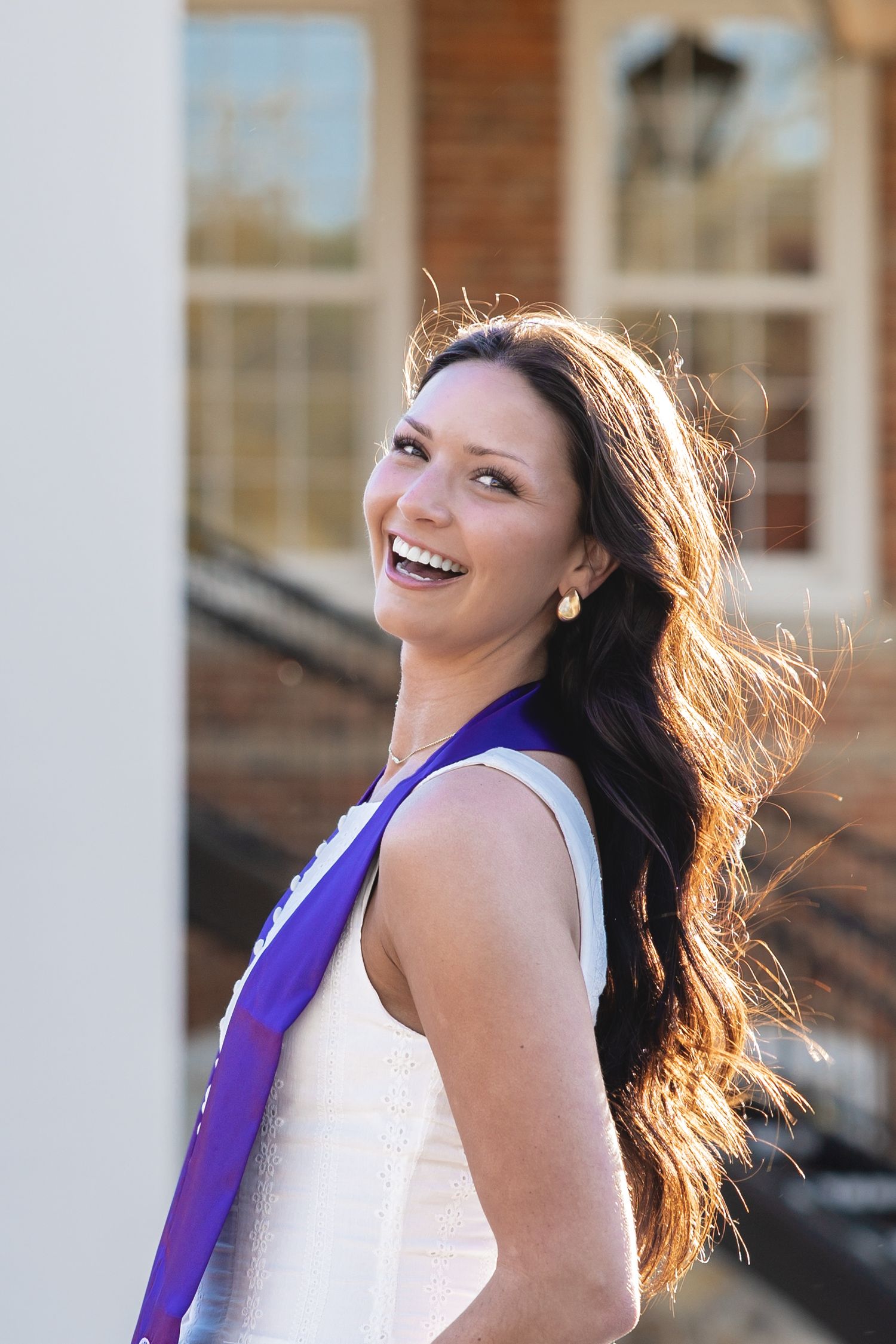 Graduate with flowing hair and purple sash posing against white columns.