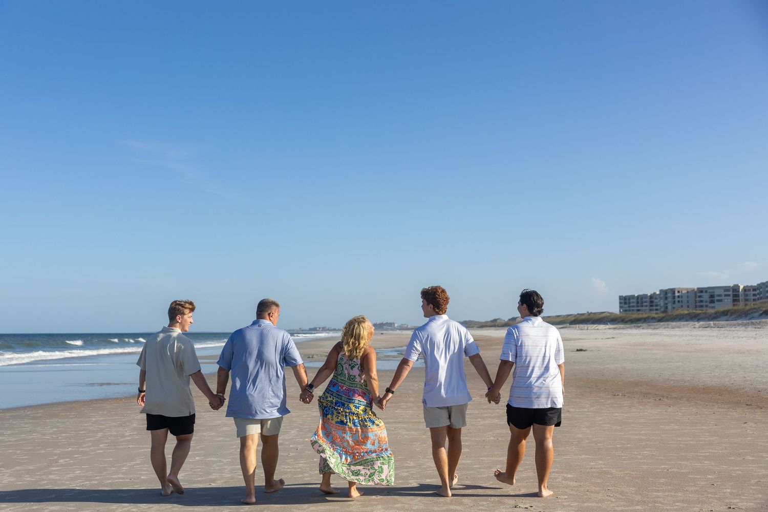 Group of people holding hands while walking together on a sandy beach with ocean waves in the background.