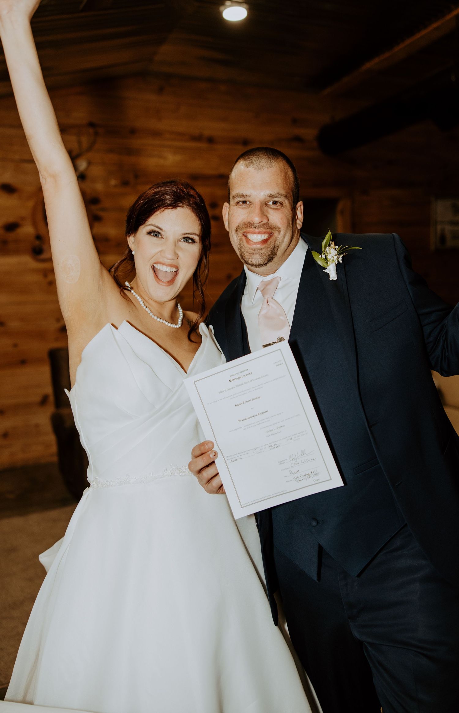 Joyful couple celebrating with marriage certificate in rustic wooden venue.