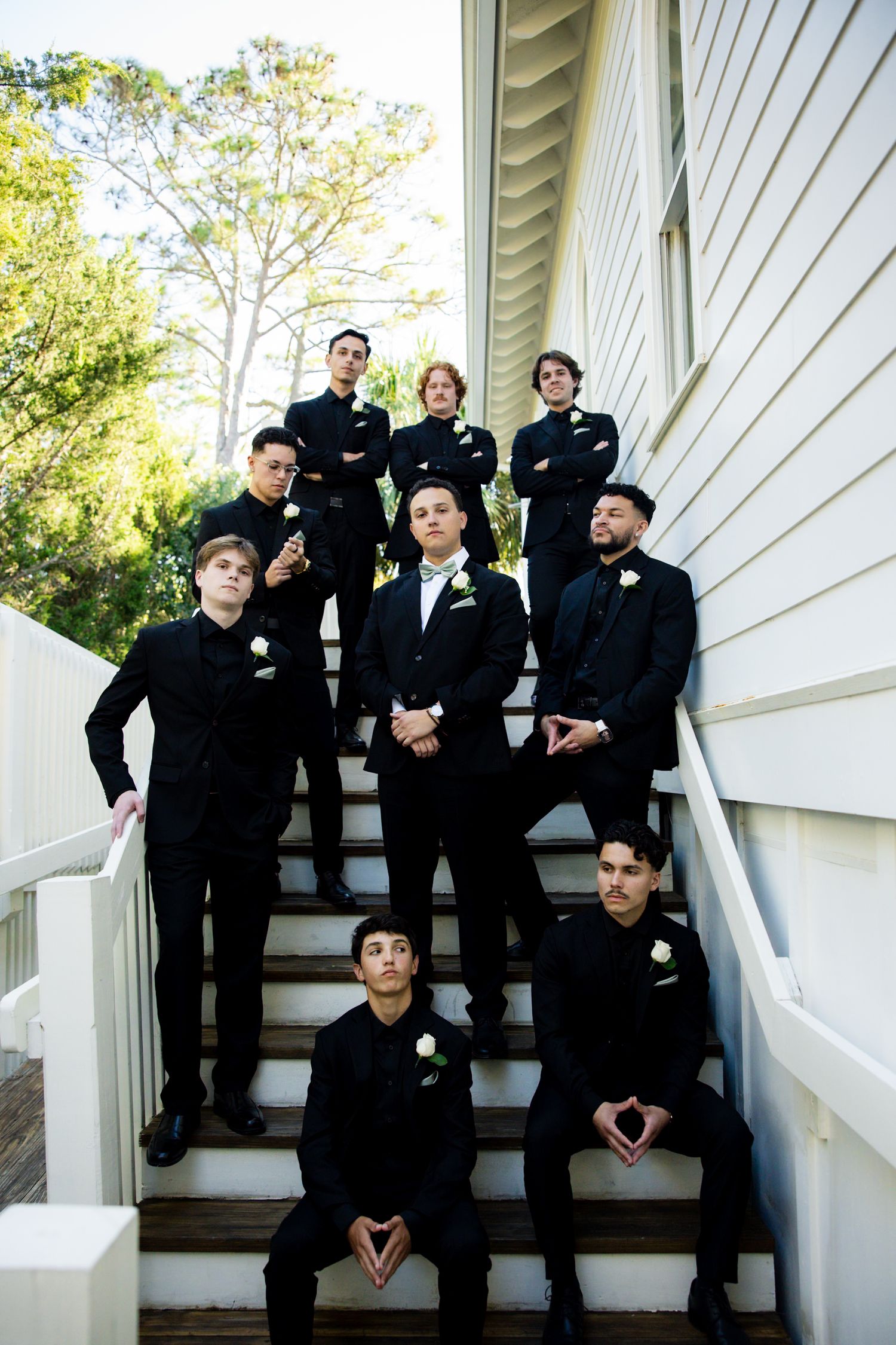 A wedding party in formal black attire poses together on white outdoor stairs in a series of candid group photos.