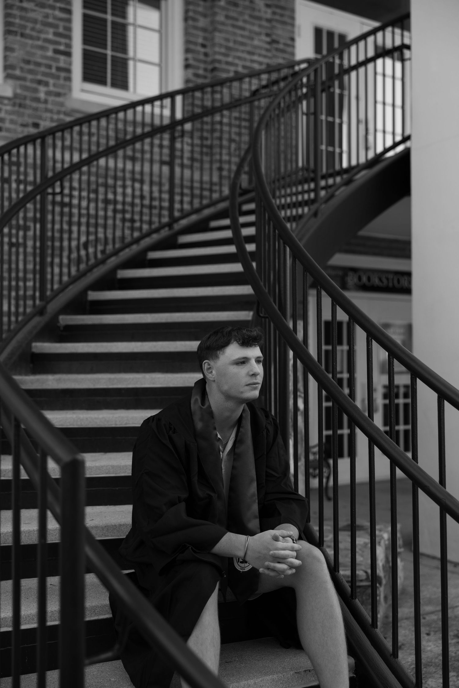 Black and white portrait of person sitting on curved staircase.