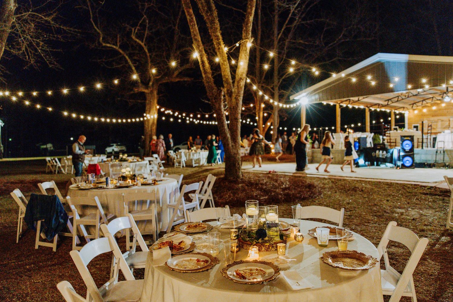 Outdoor wedding reception with string lights, round tables, and white chairs under starlit sky.