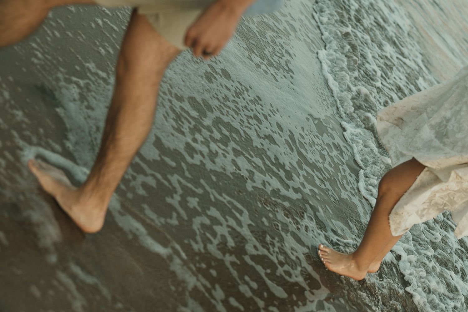 Bare legs and feet dangling over rippling water in moody teal tones from above view.