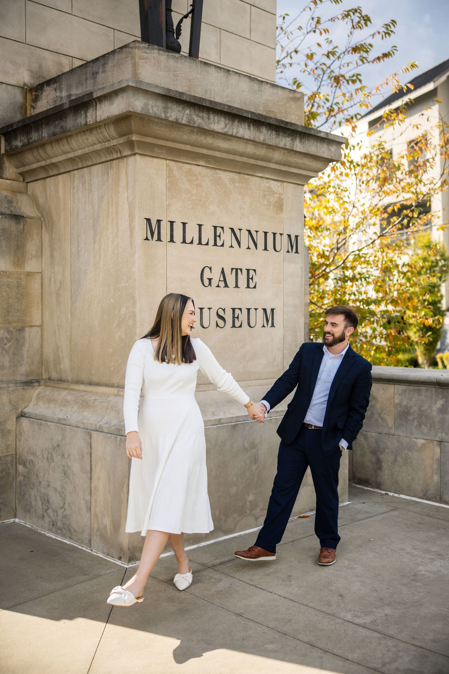 Couple holding hands in front of Millennium Gate Museum, woman in white dress and man in navy suit, Atlanta GA.