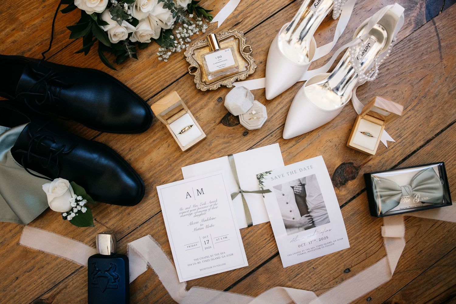Wedding details including shoes, invitations, perfume and photographs arranged on a wooden floor.