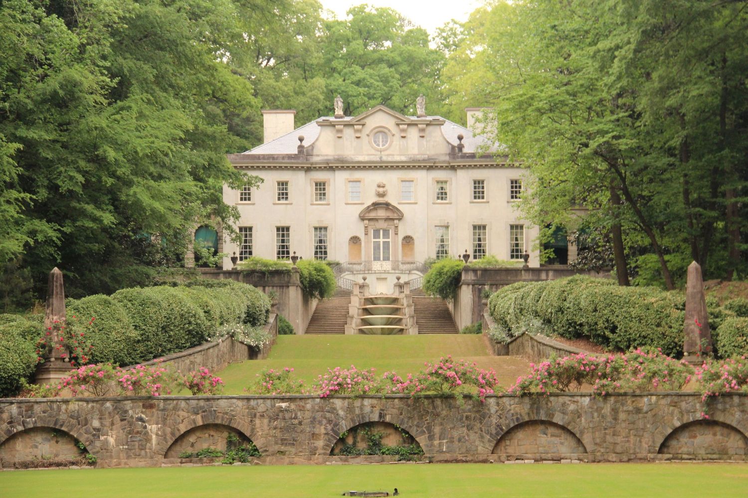 Historic stone bridge and mansion with manicured gardens creates an elegant architectural landscape at sunset.