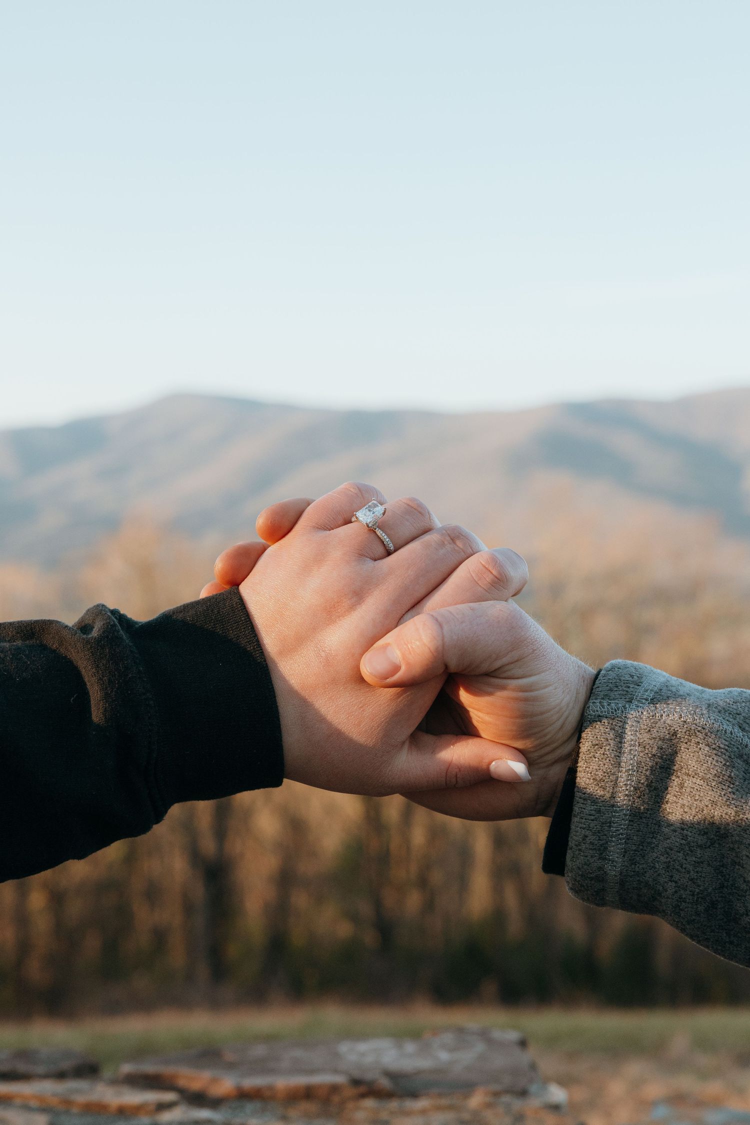 Two hands joining together with mountains in the background at sunset.