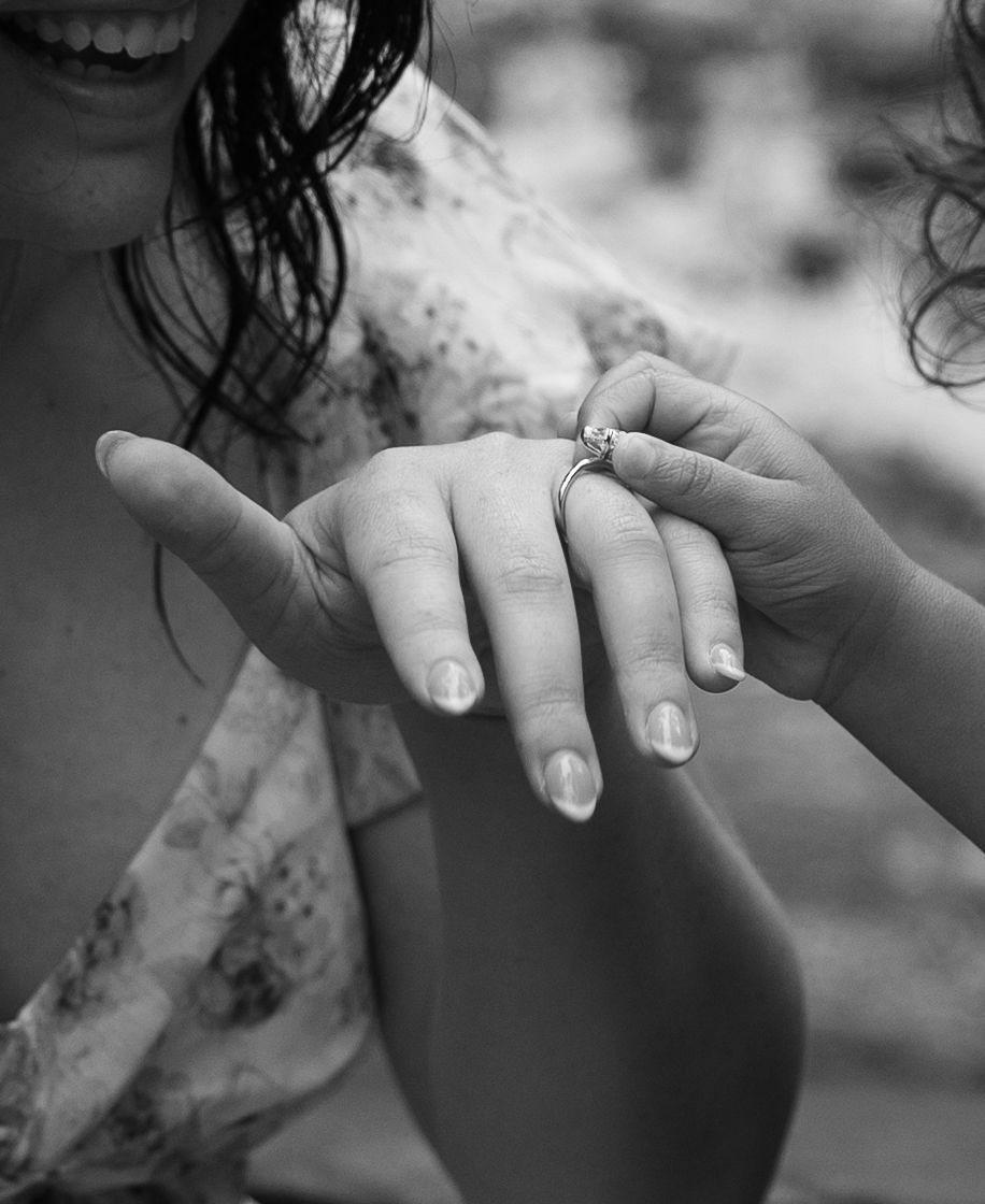 A black and white close-up of hands showing off a sparkling engagement ring.
