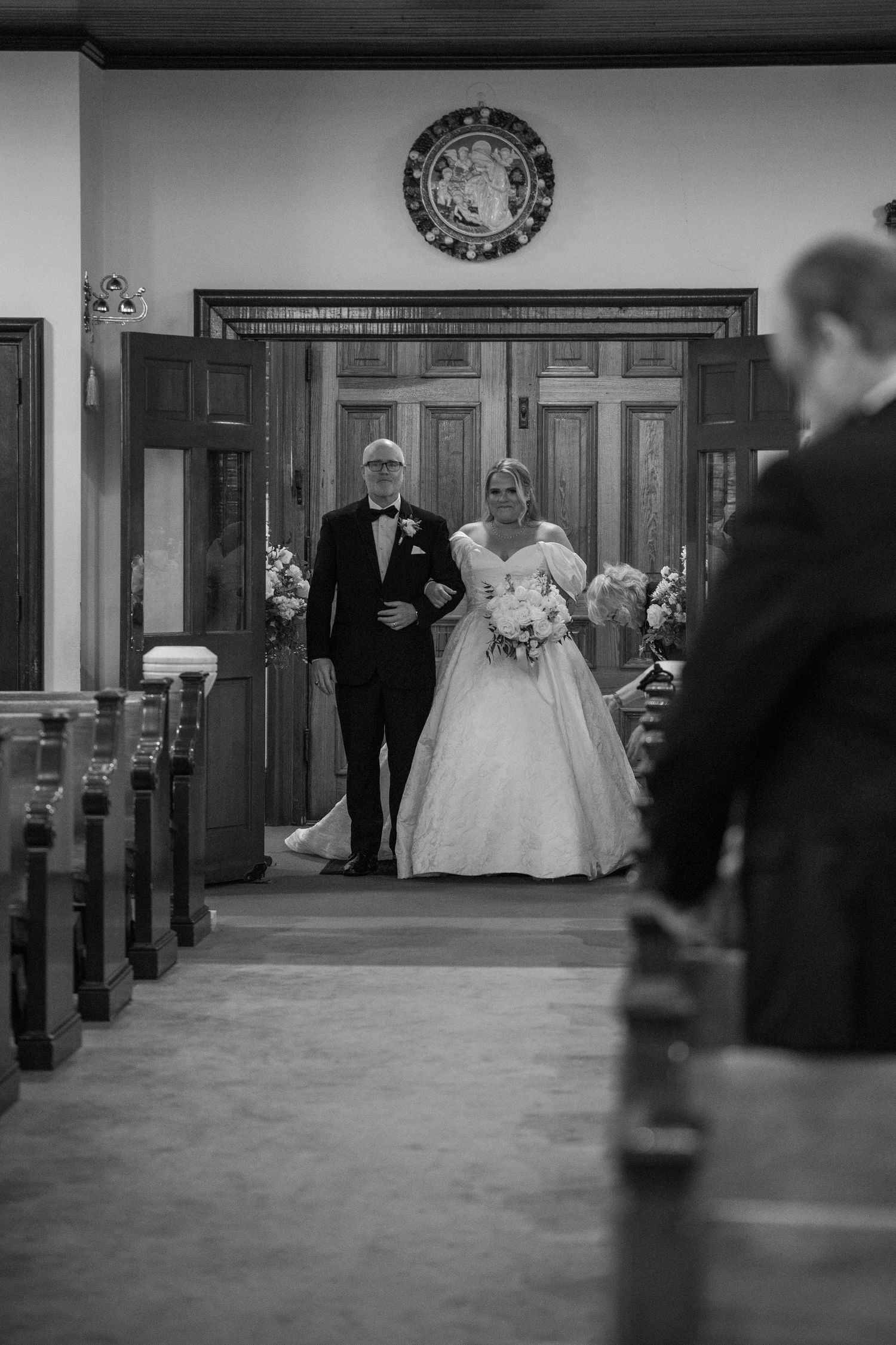 Black and white photo of a bride walking down the church aisle with her father during a traditional wedding ceremony.