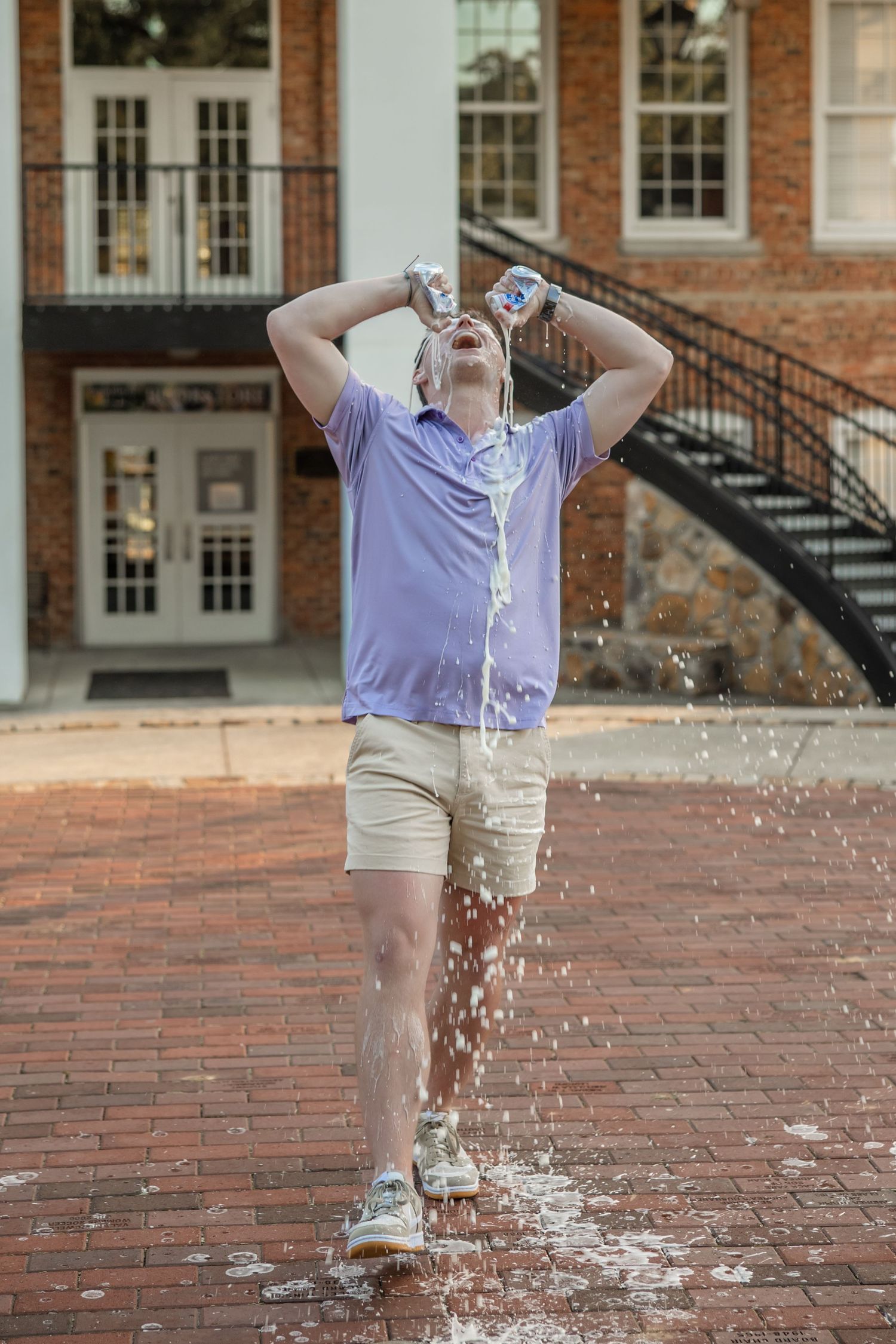 Graduate celebrating on brick courtyard with confetti in front of collegiate building.