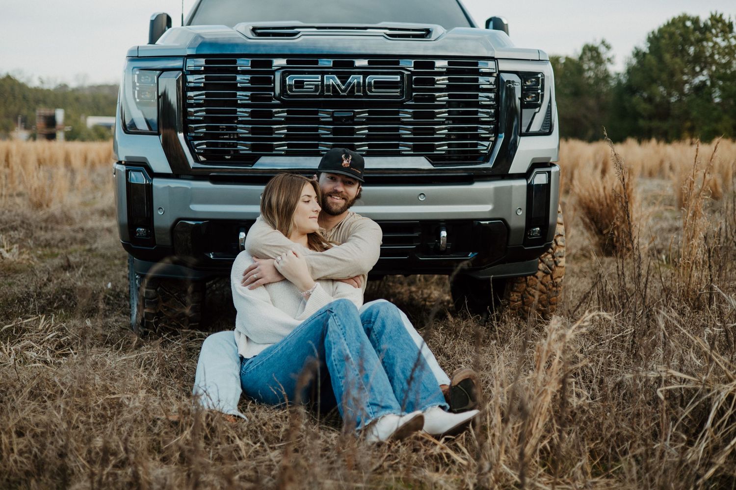 A couple sitting together by their GMC truck in a rustic field setting.