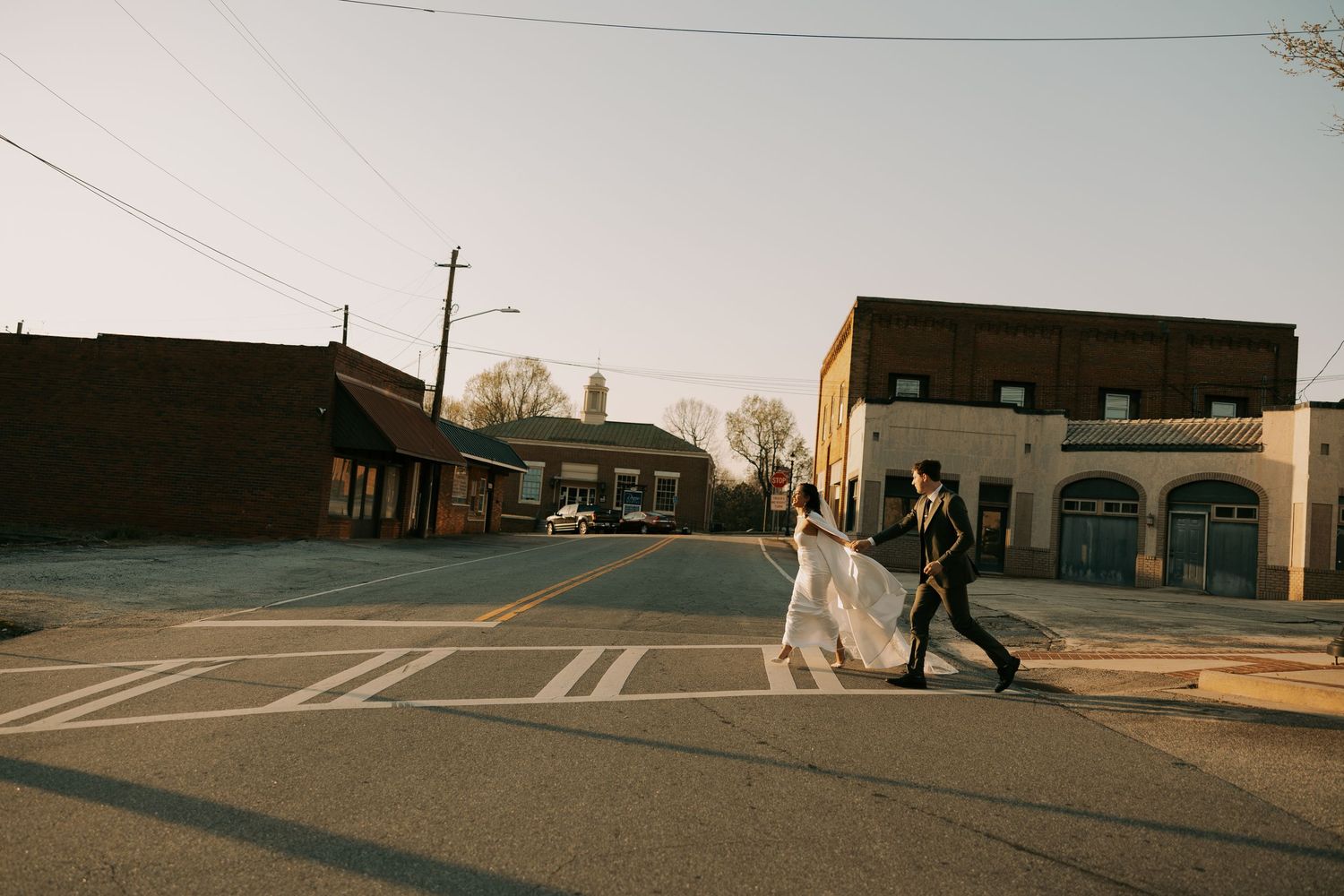 Wedding couple crosses empty street in urban setting at dusk.