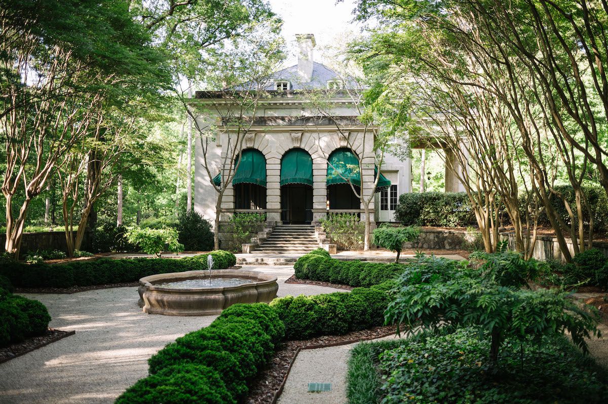 A winding garden pathway leads through lush greenery to an elegant arched gazebo structure in a formal garden setting.