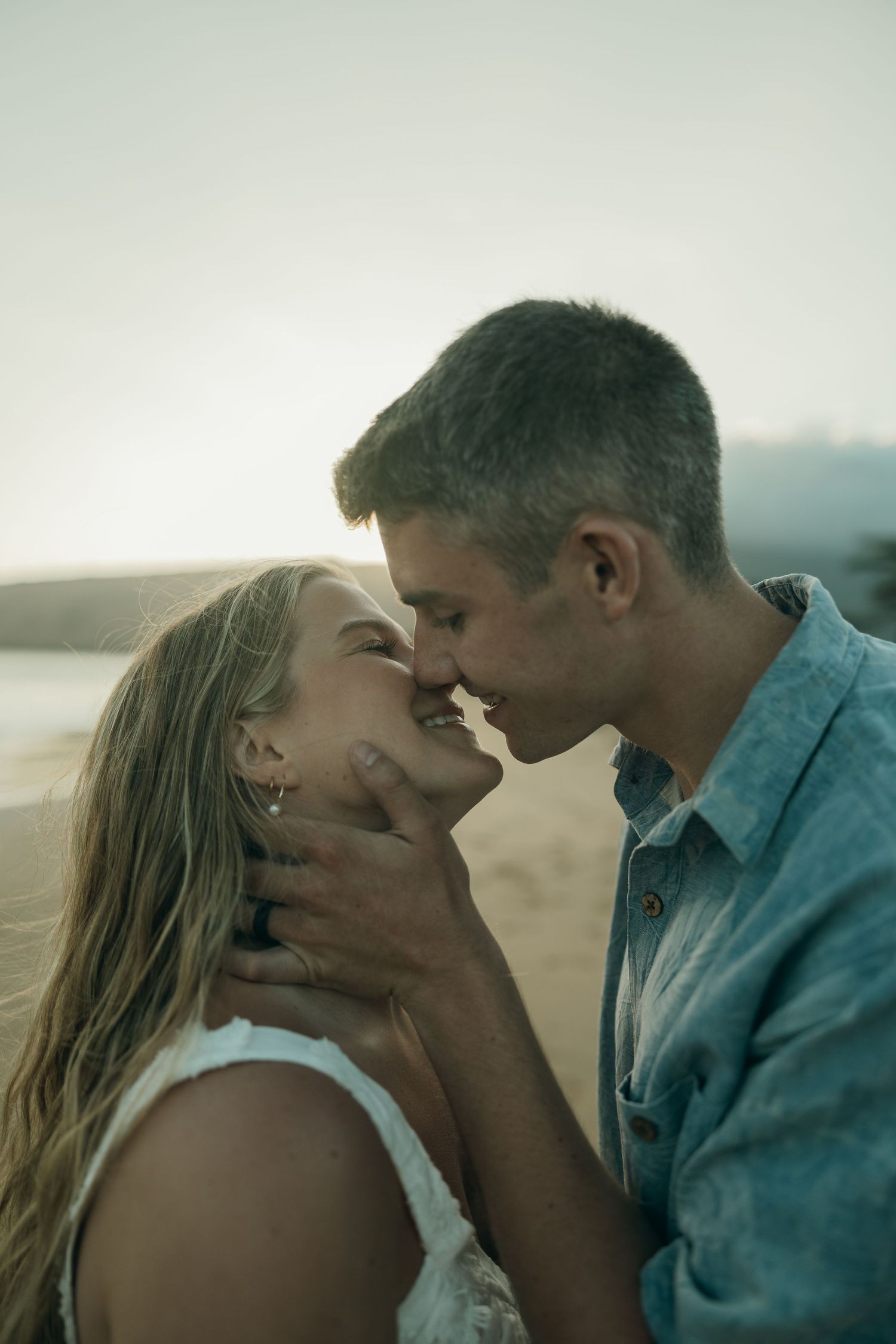 An intimate romantic moment captured between two people during golden hour on a beach.