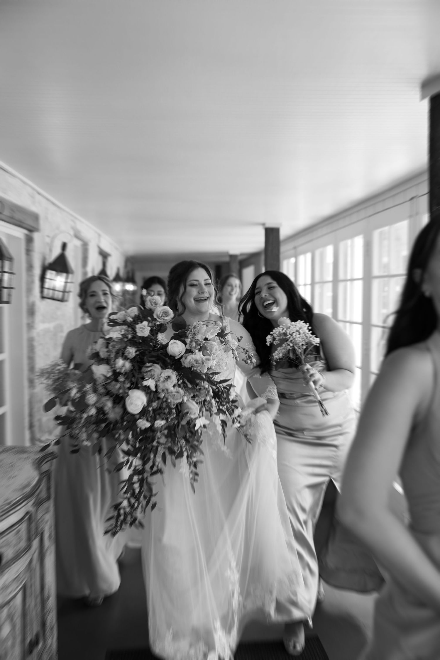 A candid black and white photo series showing a bridal party holding bouquets and laughing together in a bright room.