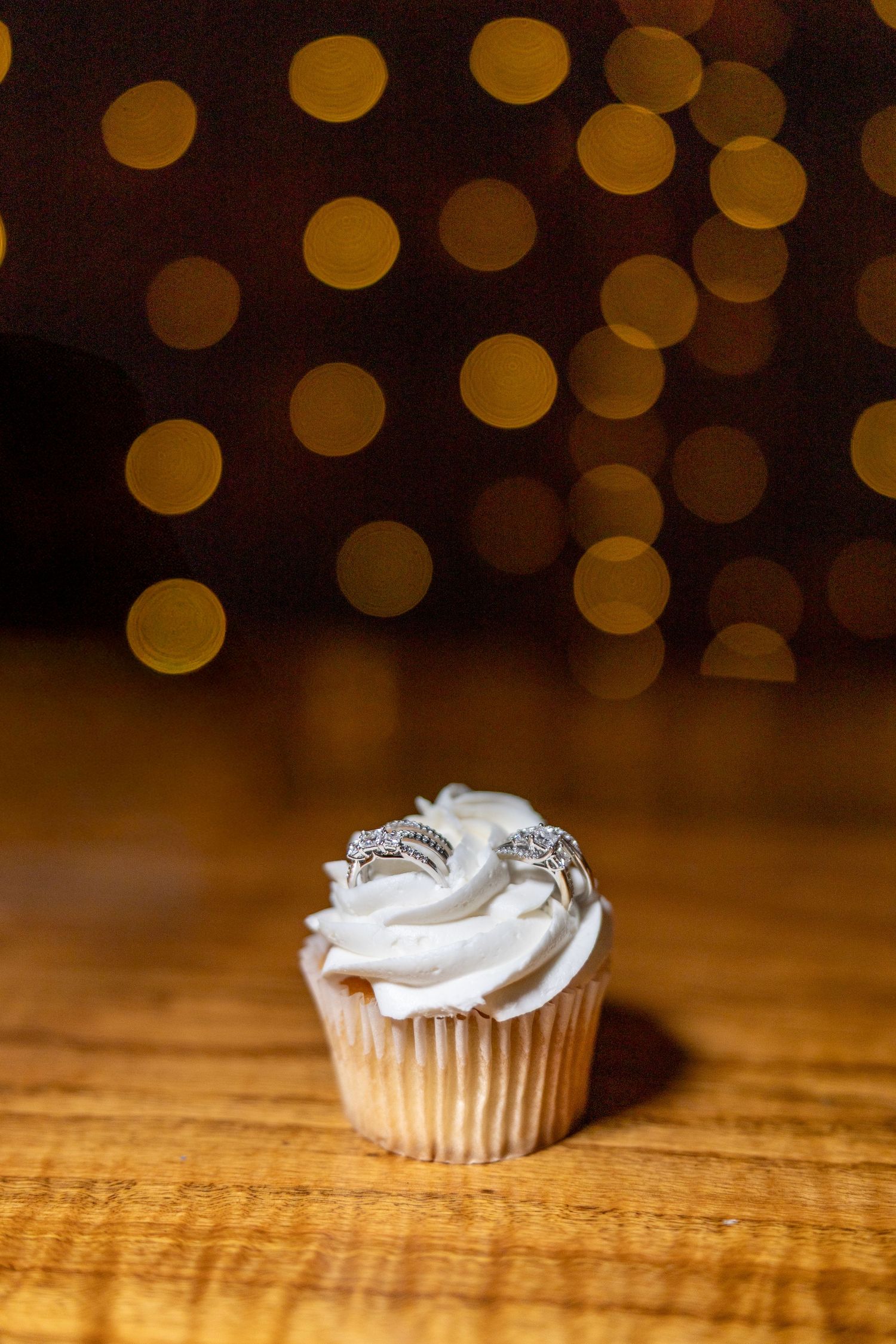 Vanilla cupcake with white frosting on wooden table with warm bokeh lights in the background.
