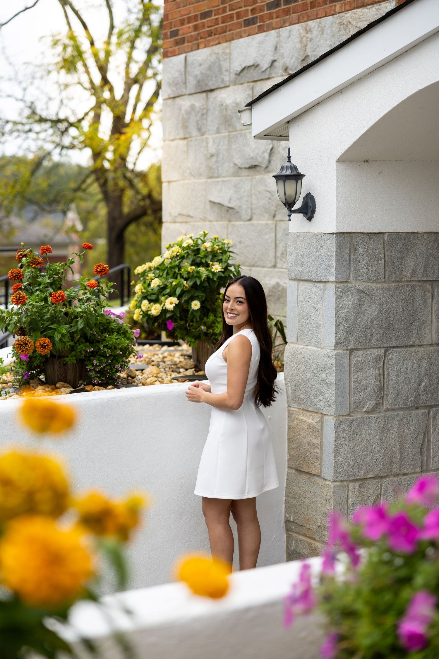 White stone porch decorated with colorful summer flowers including yellow marigolds and pink blooms in garden planters.