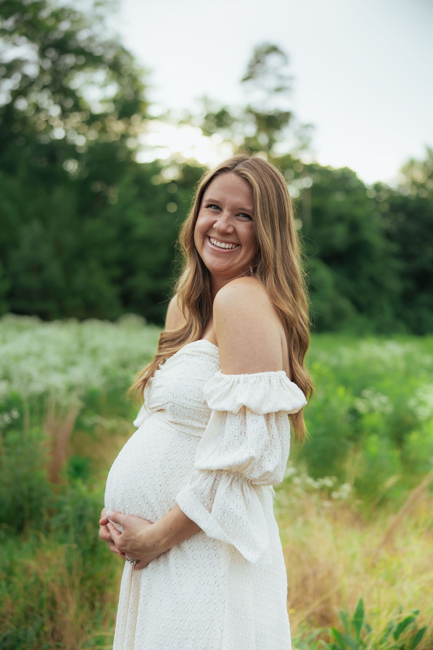A series of maternity photos showing a woman in a white dress posing in a sunny meadow with natural greenery.