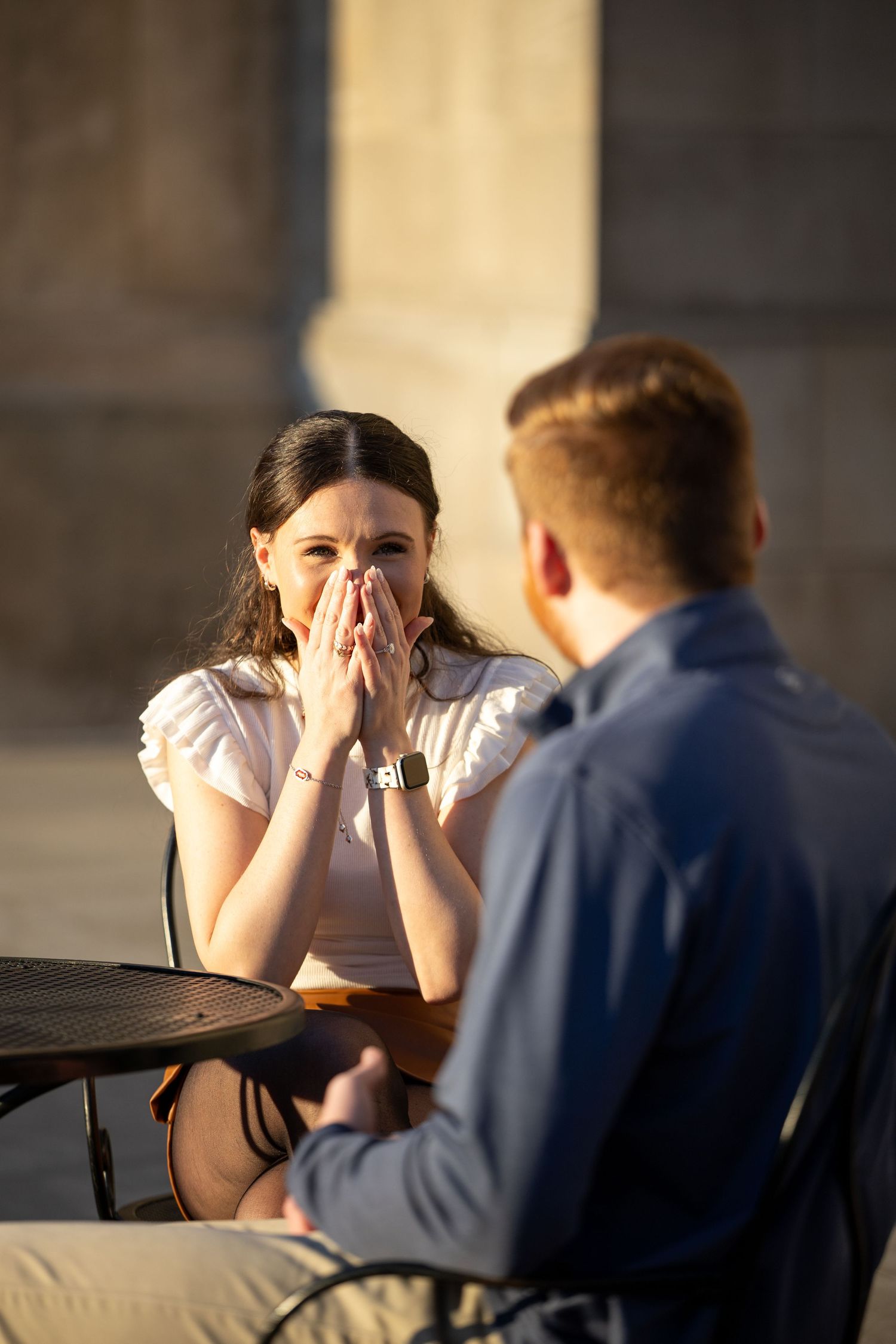 Two people sit at a table during a serious conversation as one covers their face with their hands.