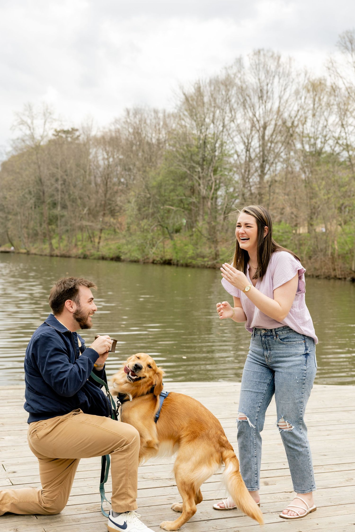 A joyful proposal moment on a dock with a golden retriever joining in the celebration.