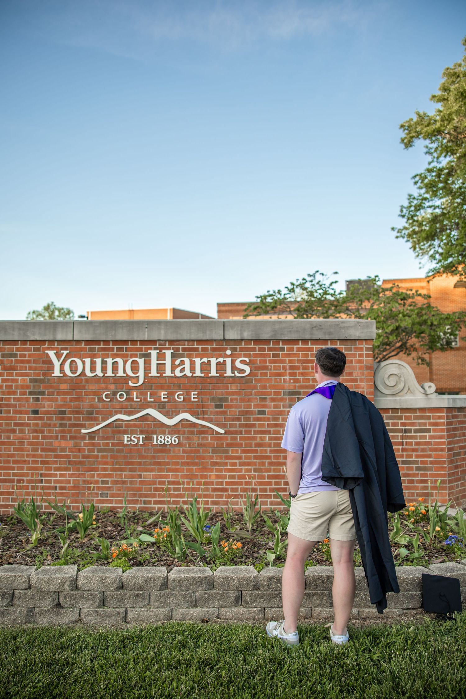 Two people walking past Young Harris College brick entrance sign.