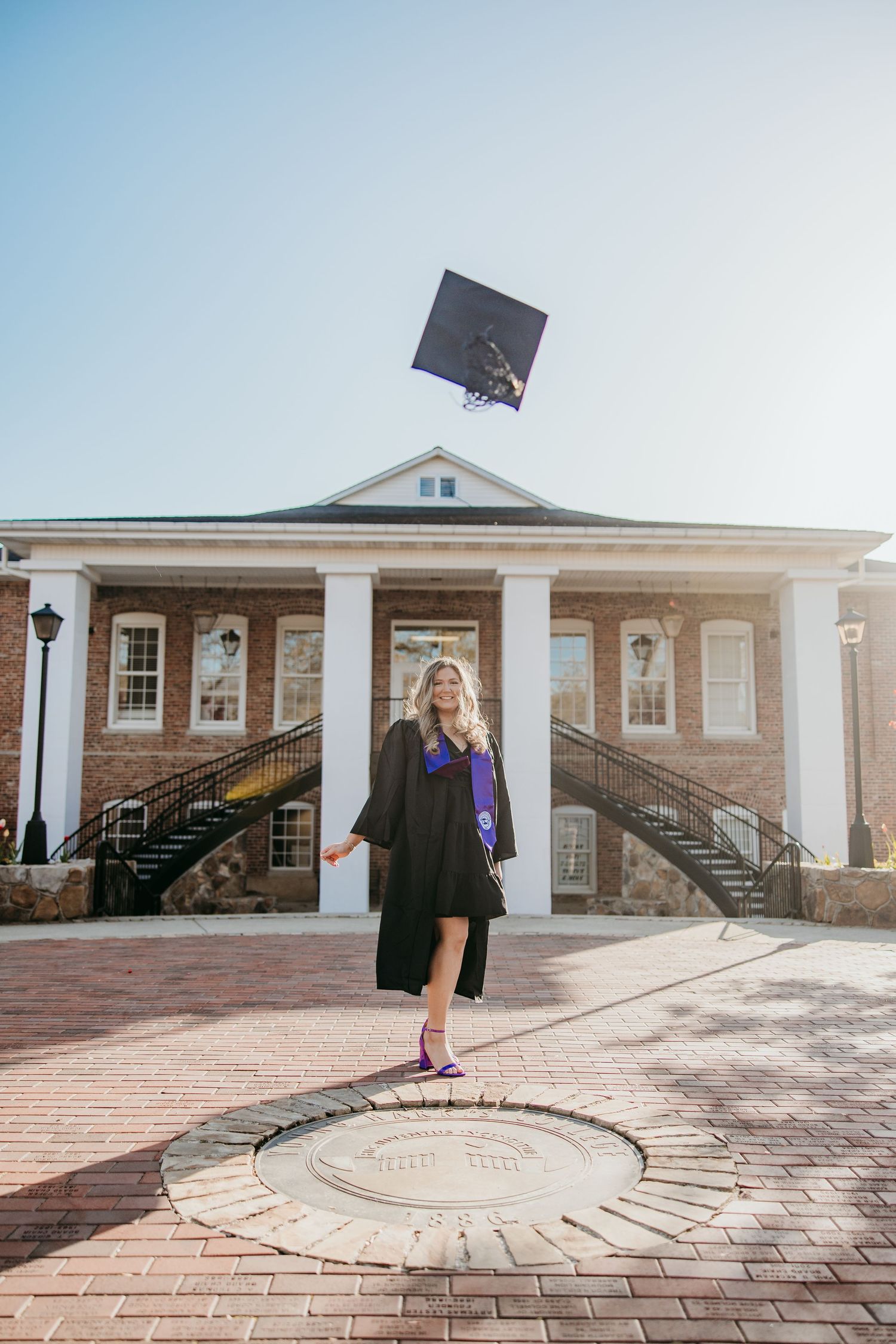 Graduation cap toss photo in front of brick colonial-style building.