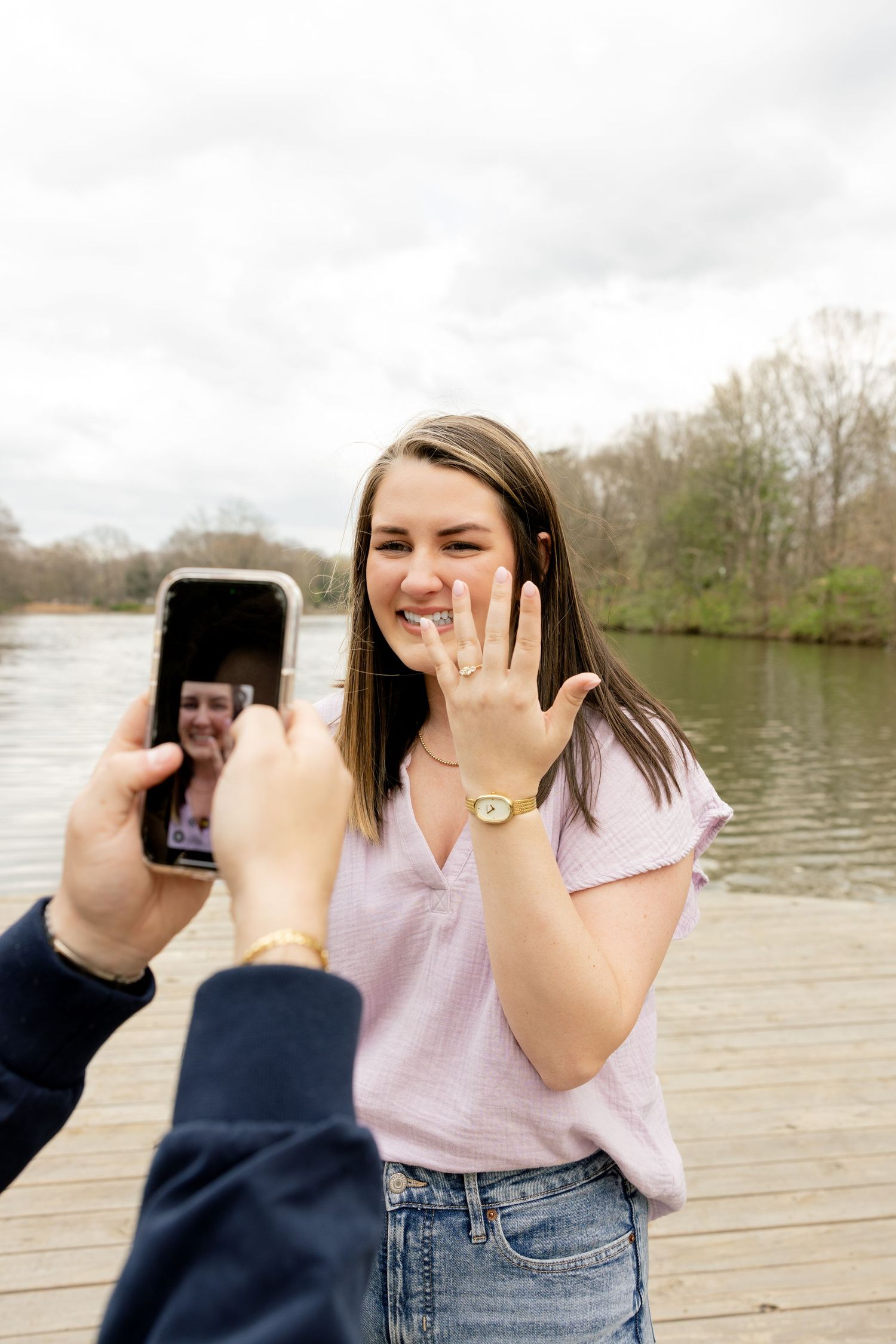 A joyful moment captured while showing off a new engagement ring on a lakeside dock.