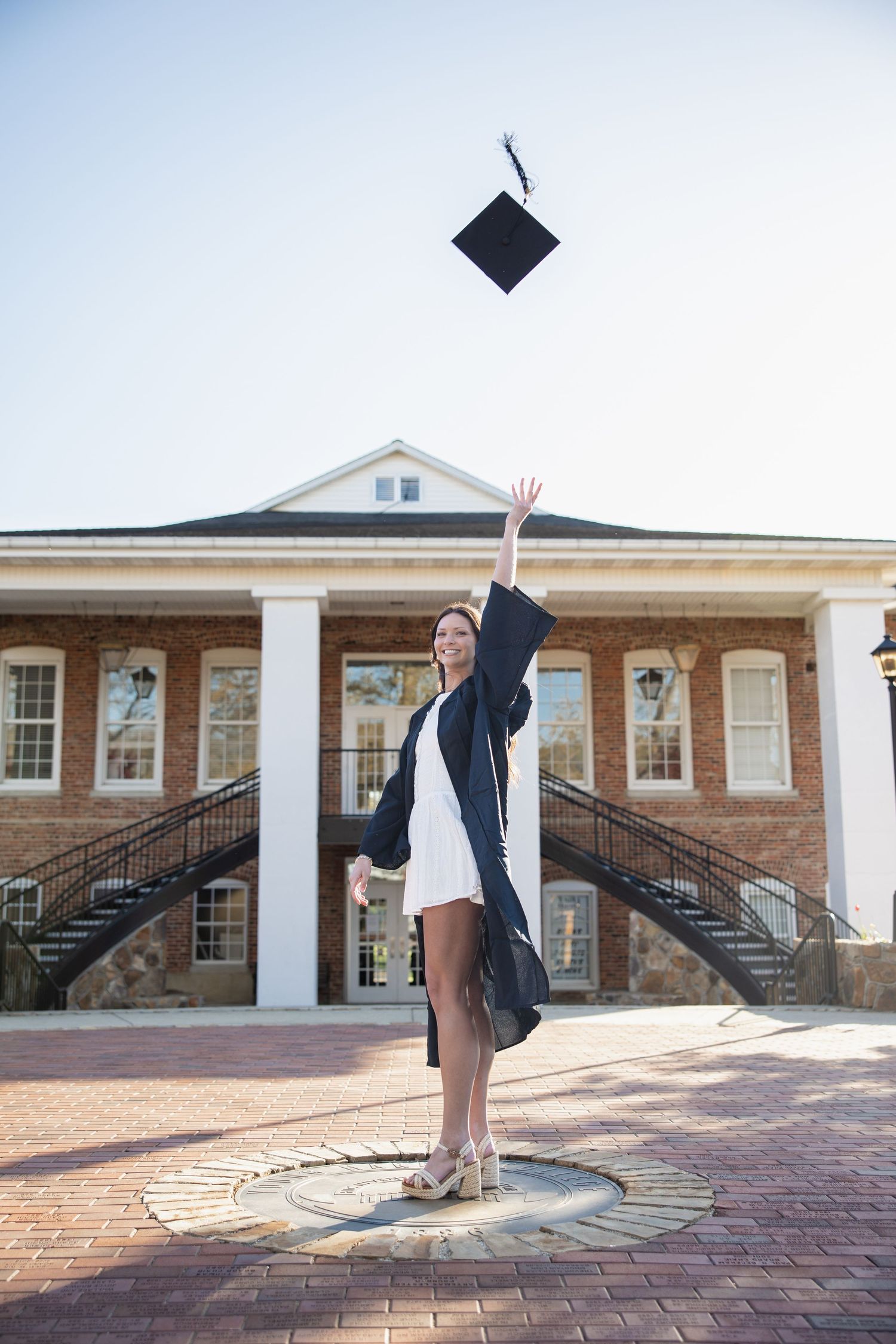 Graduate tossing graduation cap in the air on brick courtyard.