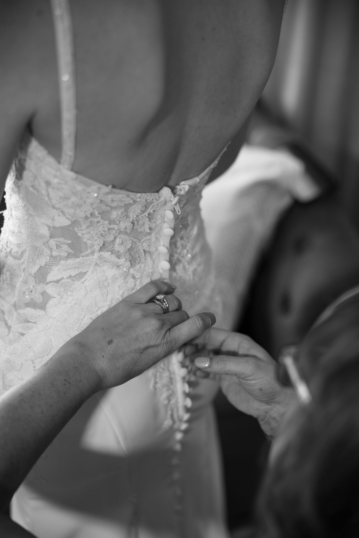 Hands with a diamond engagement ring fastening buttons on the back of a lace wedding dress.