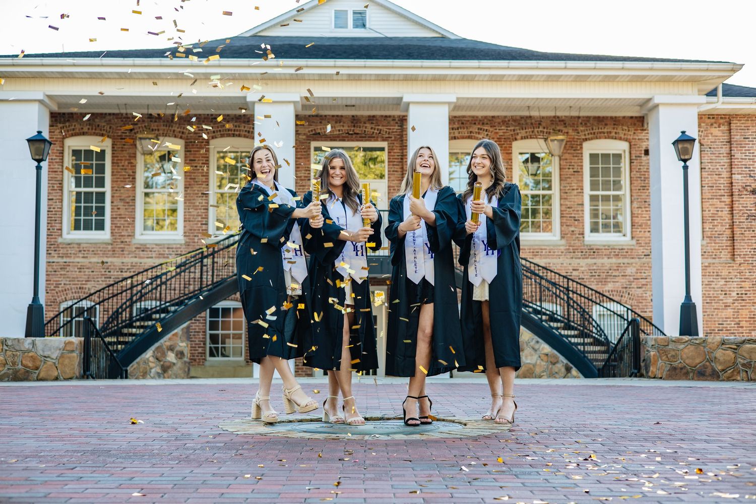 Graduates jumping with joy during celebration photo on campus steps.