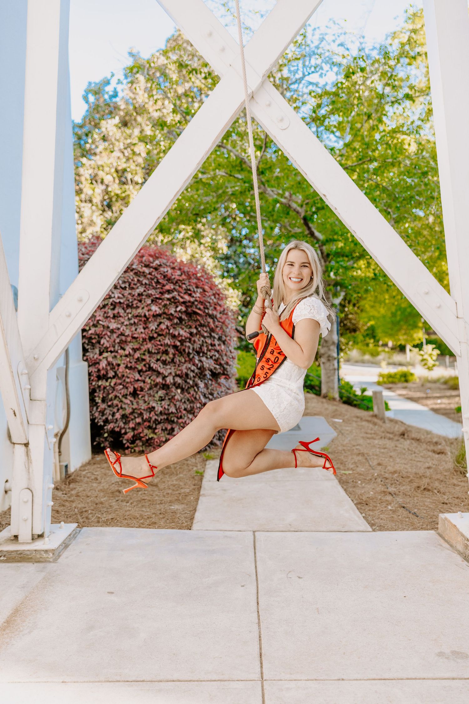 Graduate sitting on white architectural structure in graduation attire.