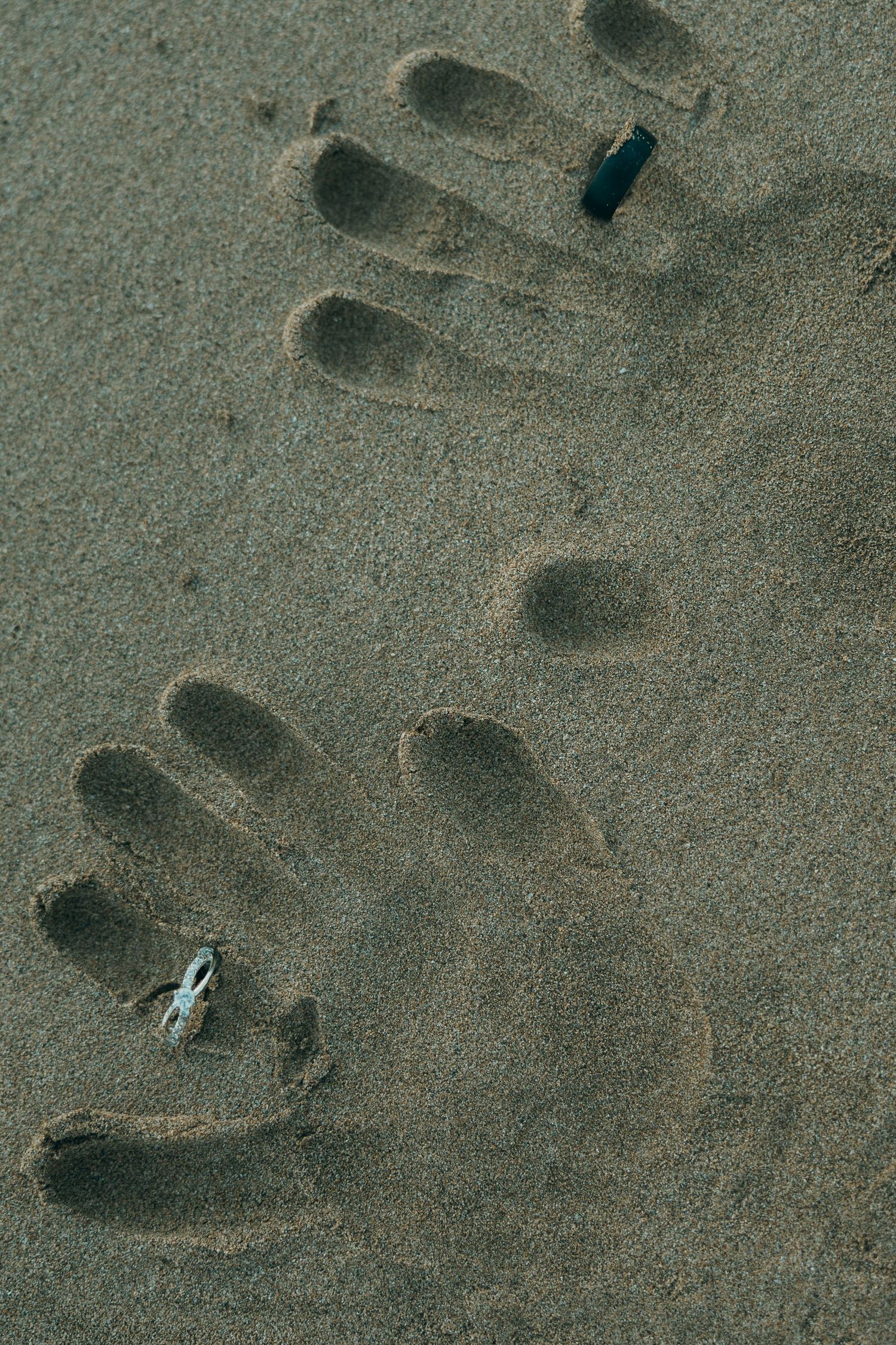 Multiple footprints scattered across dark textured sand on a beach or shoreline.