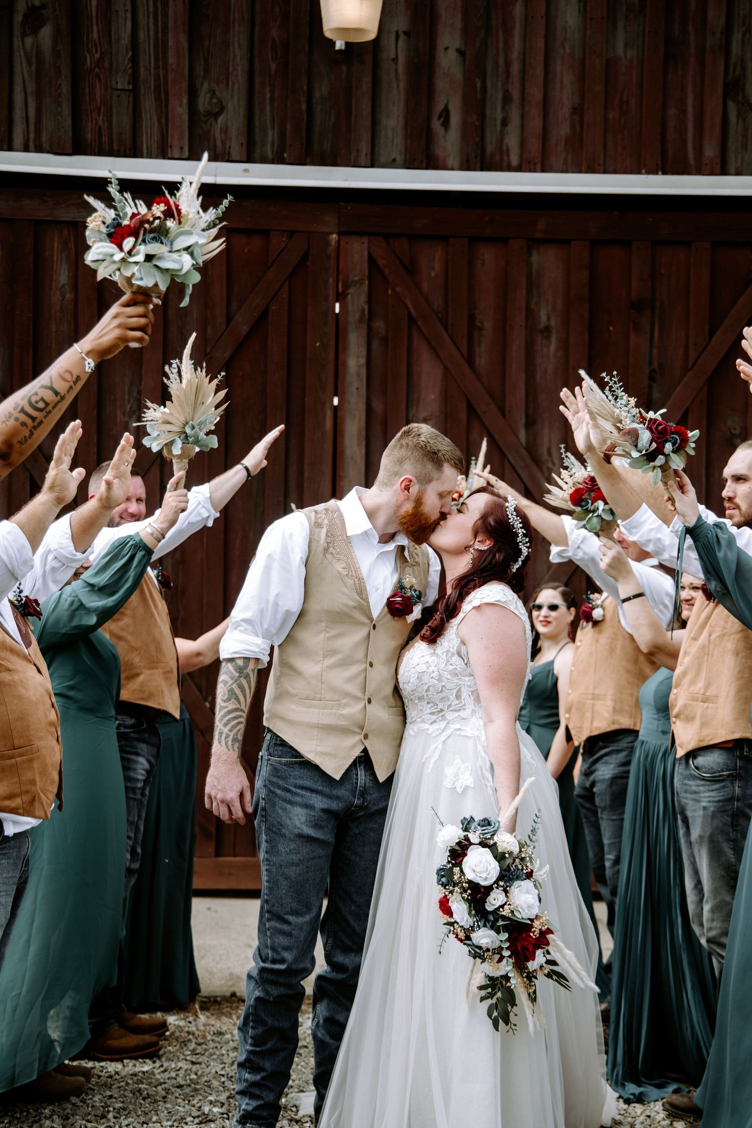 Wedding party poses with raised arms in celebration against rustic barn backdrop.