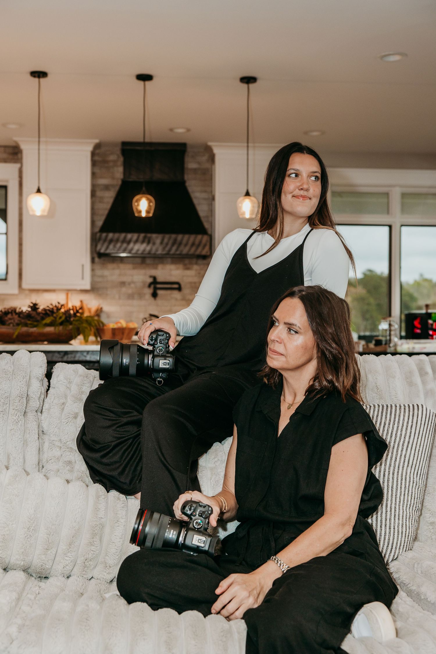 Two photographers with professional cameras relaxing on white couch in modern kitchen.