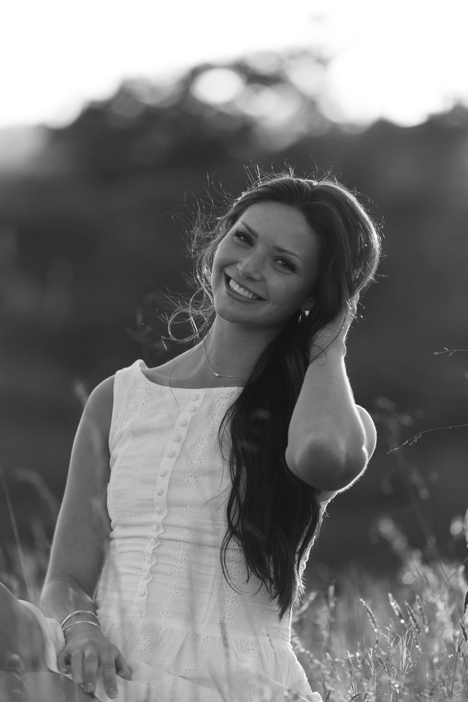 Black and white portrait of woman in white dress smiling in sunlit field.