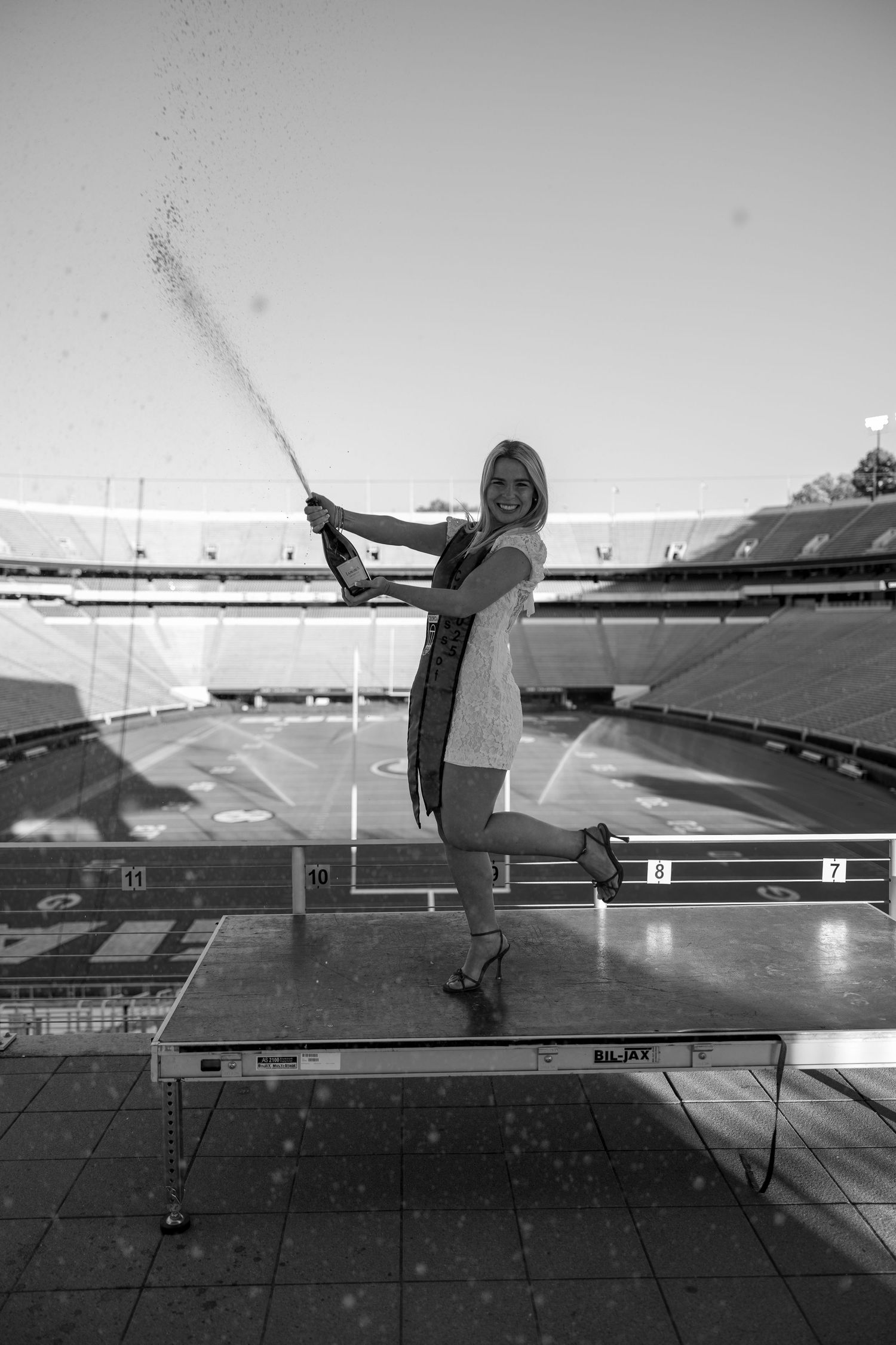 Graduate celebrating with champagne spray in stadium black and white photo.