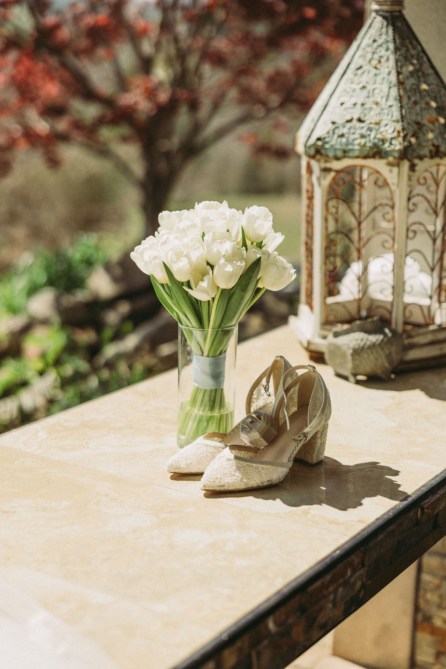 White tulip bouquet with sparkly bridal shoes and vintage lantern on stone table.