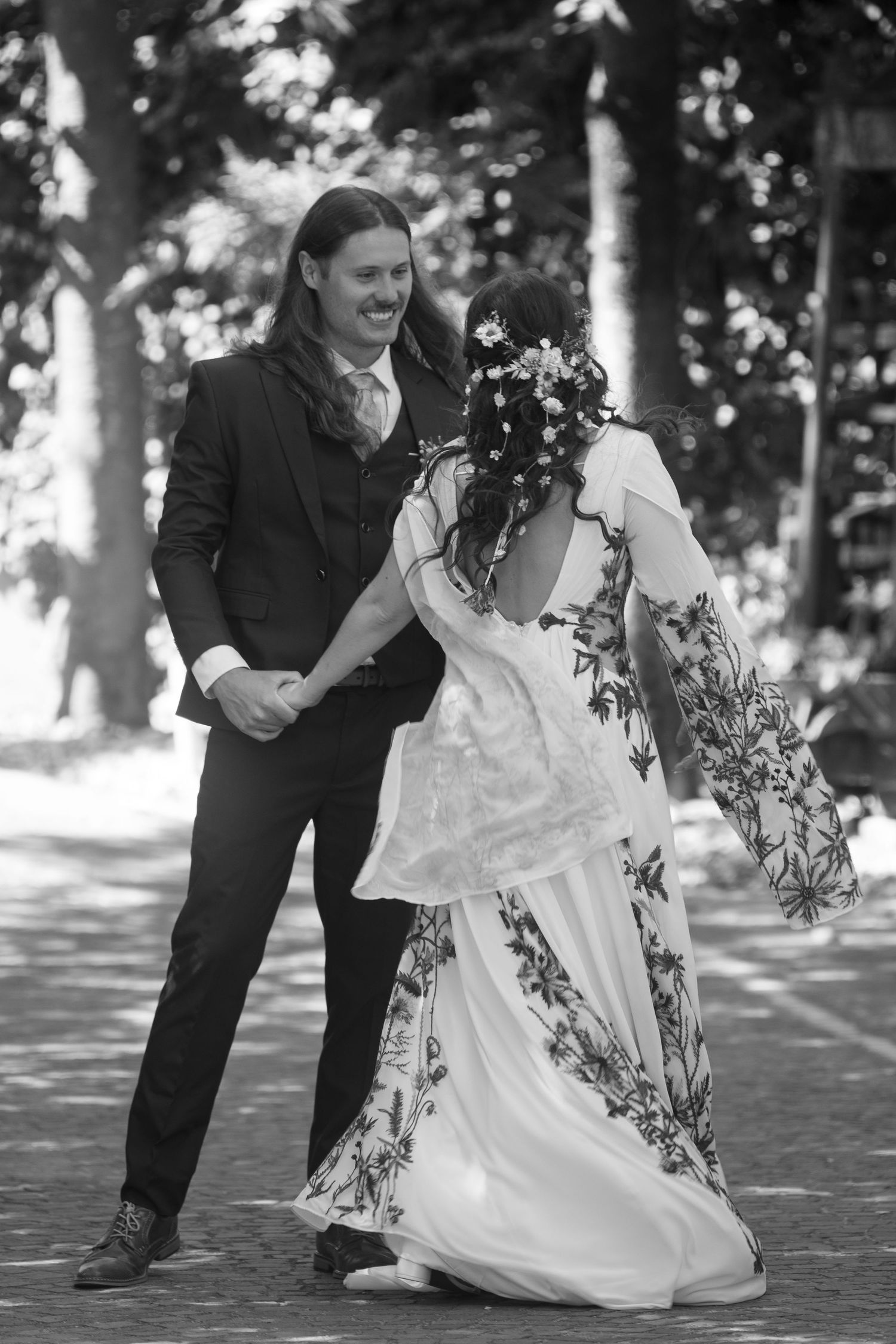 Black and white photo of bride and groom dancing outdoors under trees. Tuscany wedding photographer, filmmaker