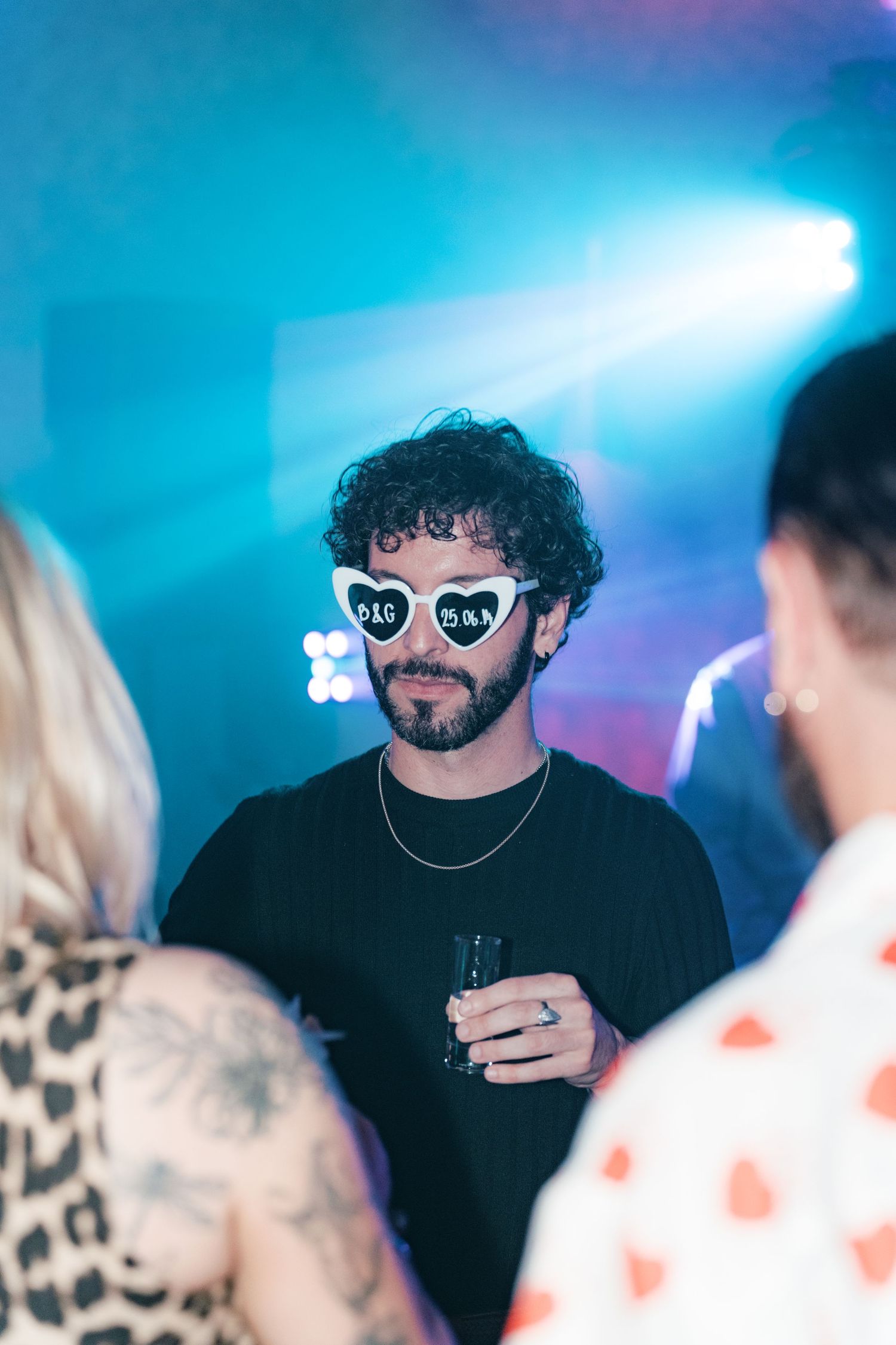 Bearded man in black shirt wearing D&G heart sunglasses at colorful party. Italy wedding photographer